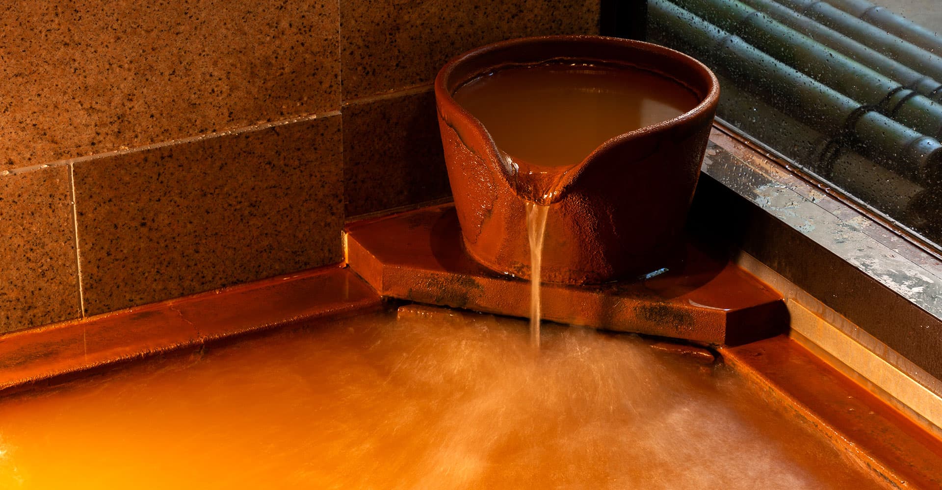Arima Onsen Koki gold-spring (kinsen) bath with steaming reddish-brown mineral water flowing from a ceramic dipper