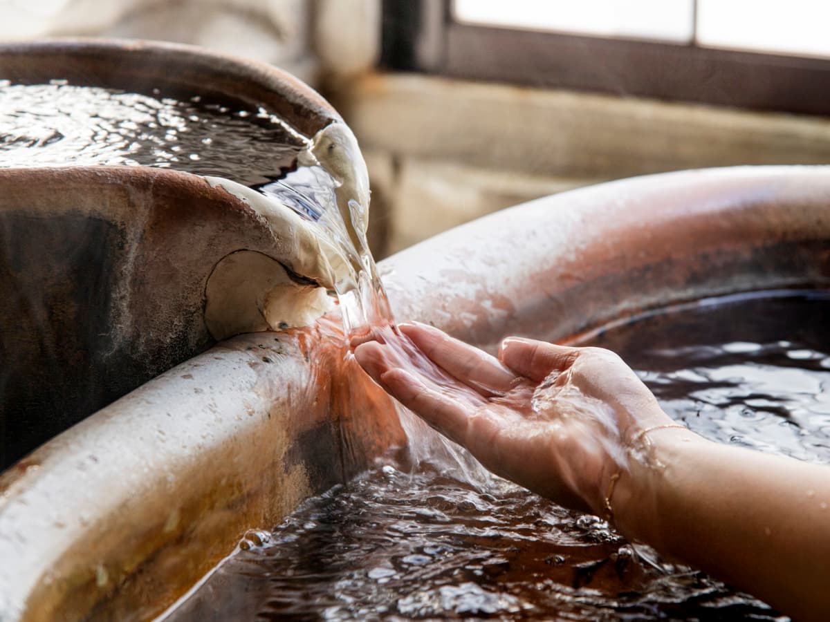 Close-up detail of Arima spring water flowing over a hand at the Koki bath source basin
