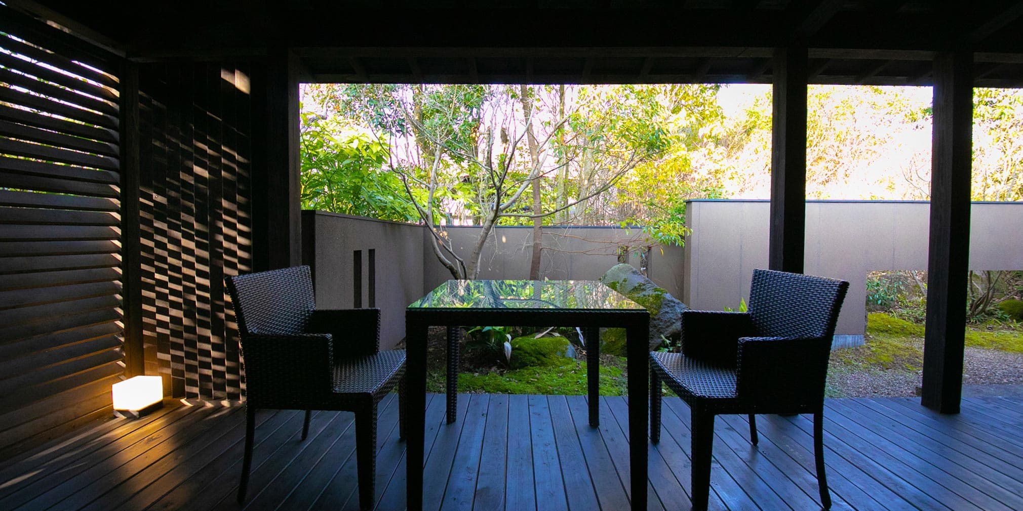 Private covered terrace with table and chairs overlooking a moss-and-tree garden at Yufuin Bettei Itsuki