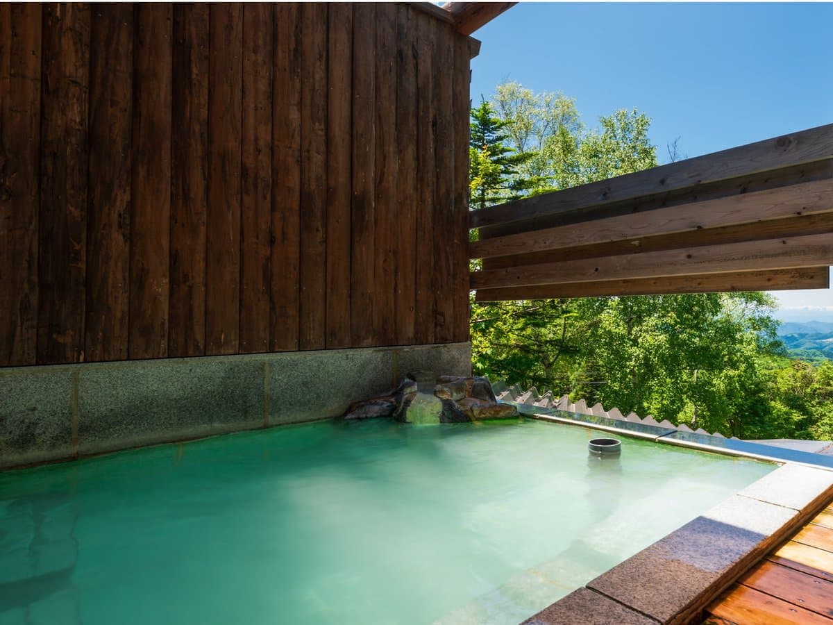 Open-air rotenburo bath with milky green sulphur water and forested mountain view at Zenshichinoyu Ohira, Zao Onsen