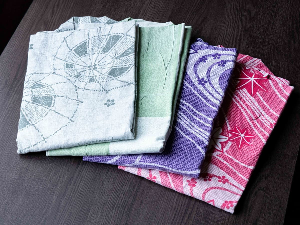 Folded patterned yukata robes arranged on a dark wood surface at Zenshichinoyu Ohira, Zao Onsen