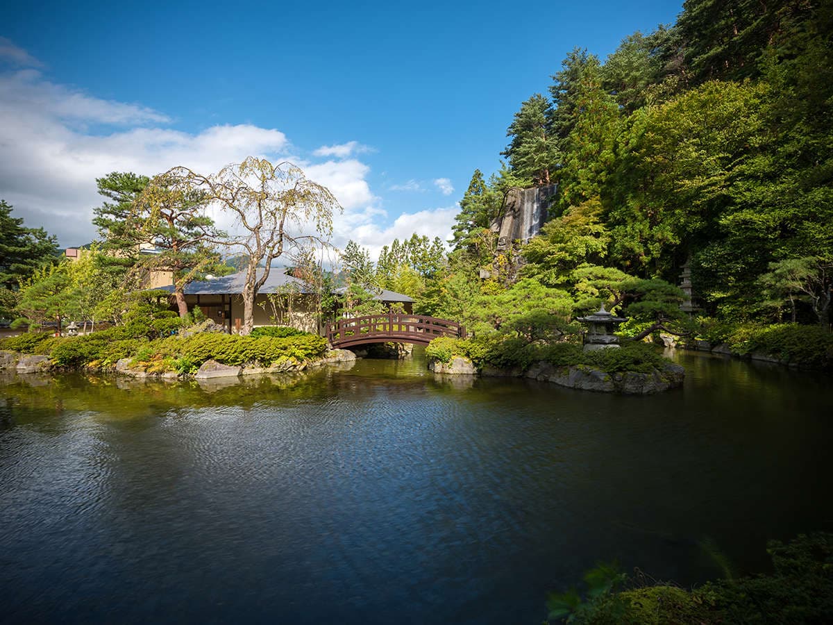 Landscaped Japanese garden with a curved stone bridge, pine trees and reflecting pond, Yumoto Kissho, Naruko Onsen