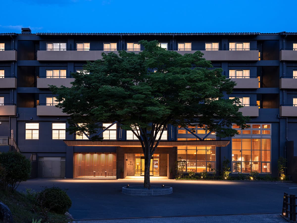Seiunso ryokan exterior at dusk in Unzen Onsen, warm-lit entrance framed by a large maple tree