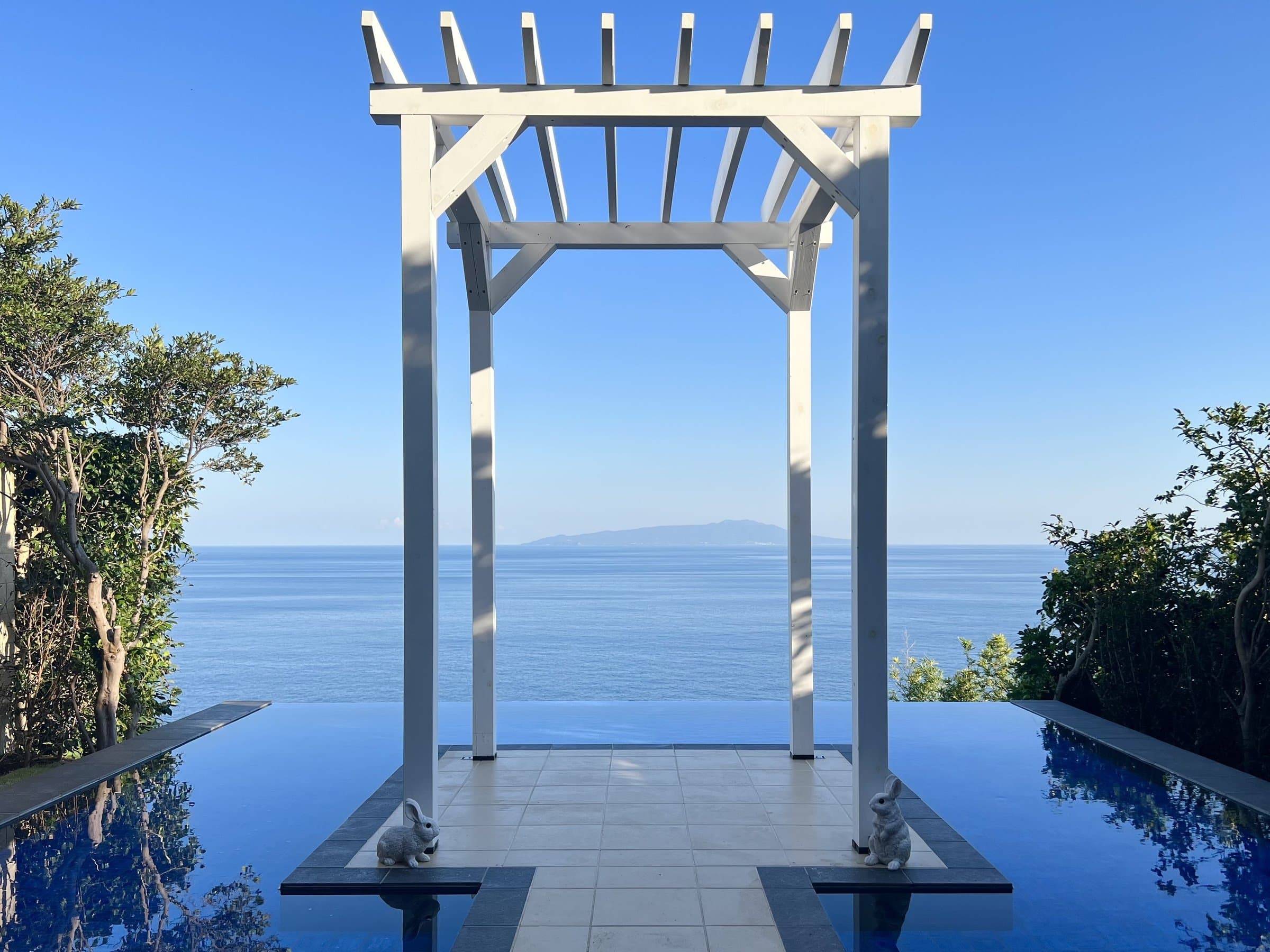 White pergola over a reflective infinity water terrace facing the ocean horizon at Tsuki no Usagi, Izu