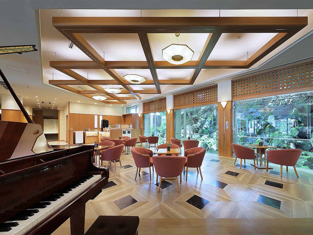 Wood-beamed lounge with a grand piano, rose-colored chairs and garden views at Zao Kokusai Hotel