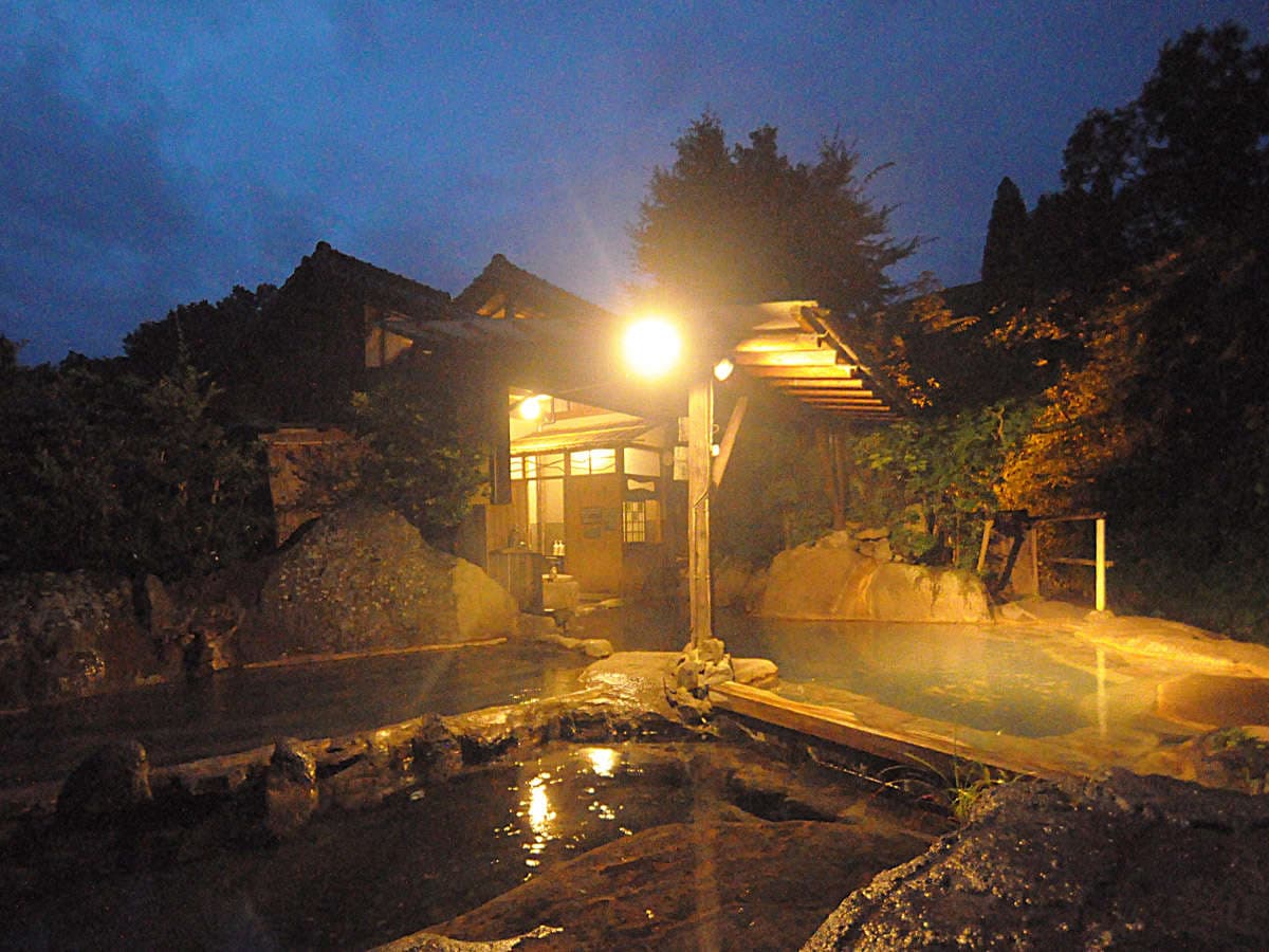 Steaming riverside open-air bath at Hozantei lit by a lantern on a misty night