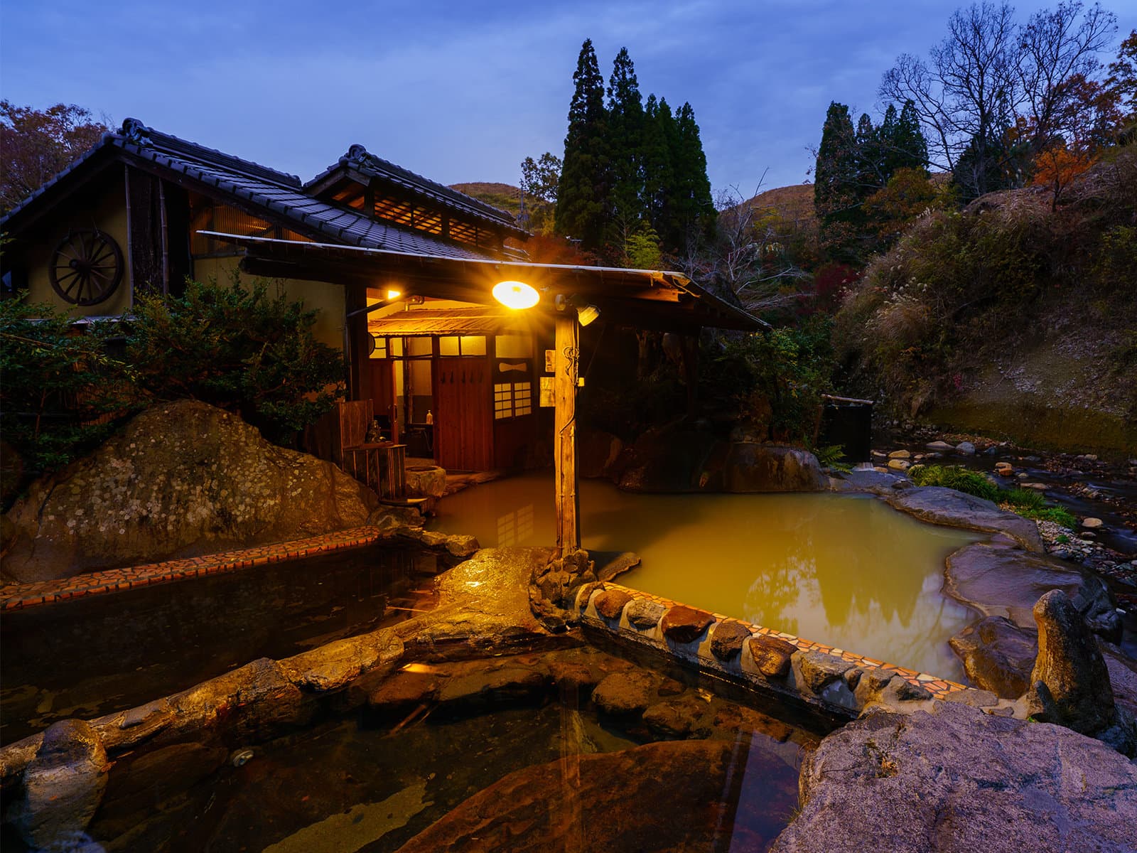 Genryu no Yado Hozantei riverside open-air bath and lantern-lit timber building at dusk in Kurokawa Onsen