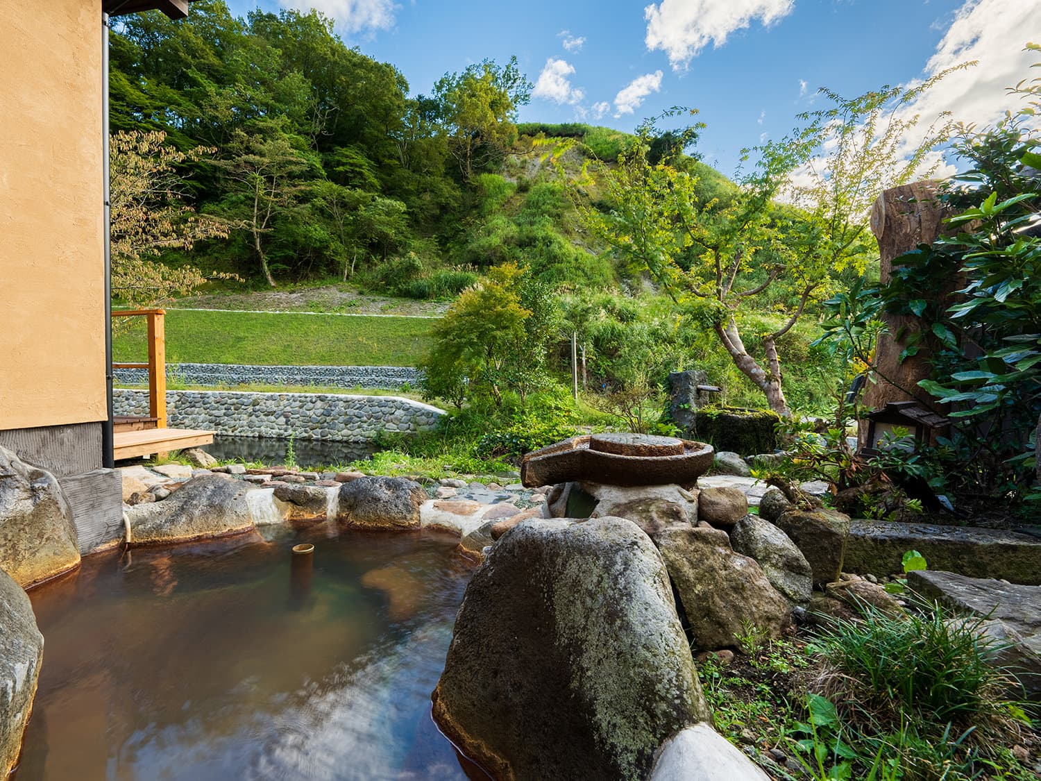 Daytime riverside open-air rotenburo at Hozantei set among rocks and garden greenery