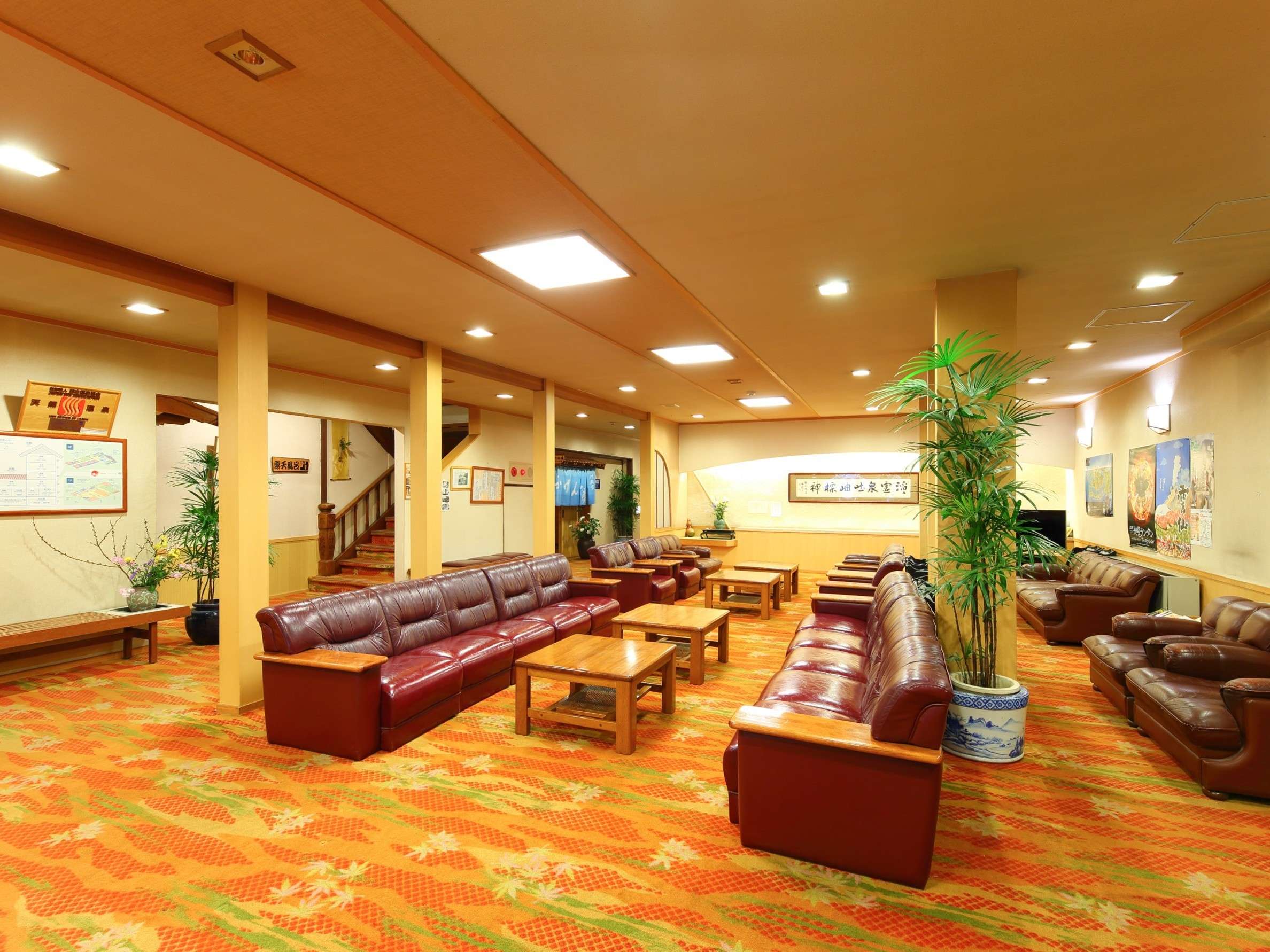 Spacious lobby lounge with leather sofas, wooden tables and a potted palm at Unzen Iwaki Ryokan