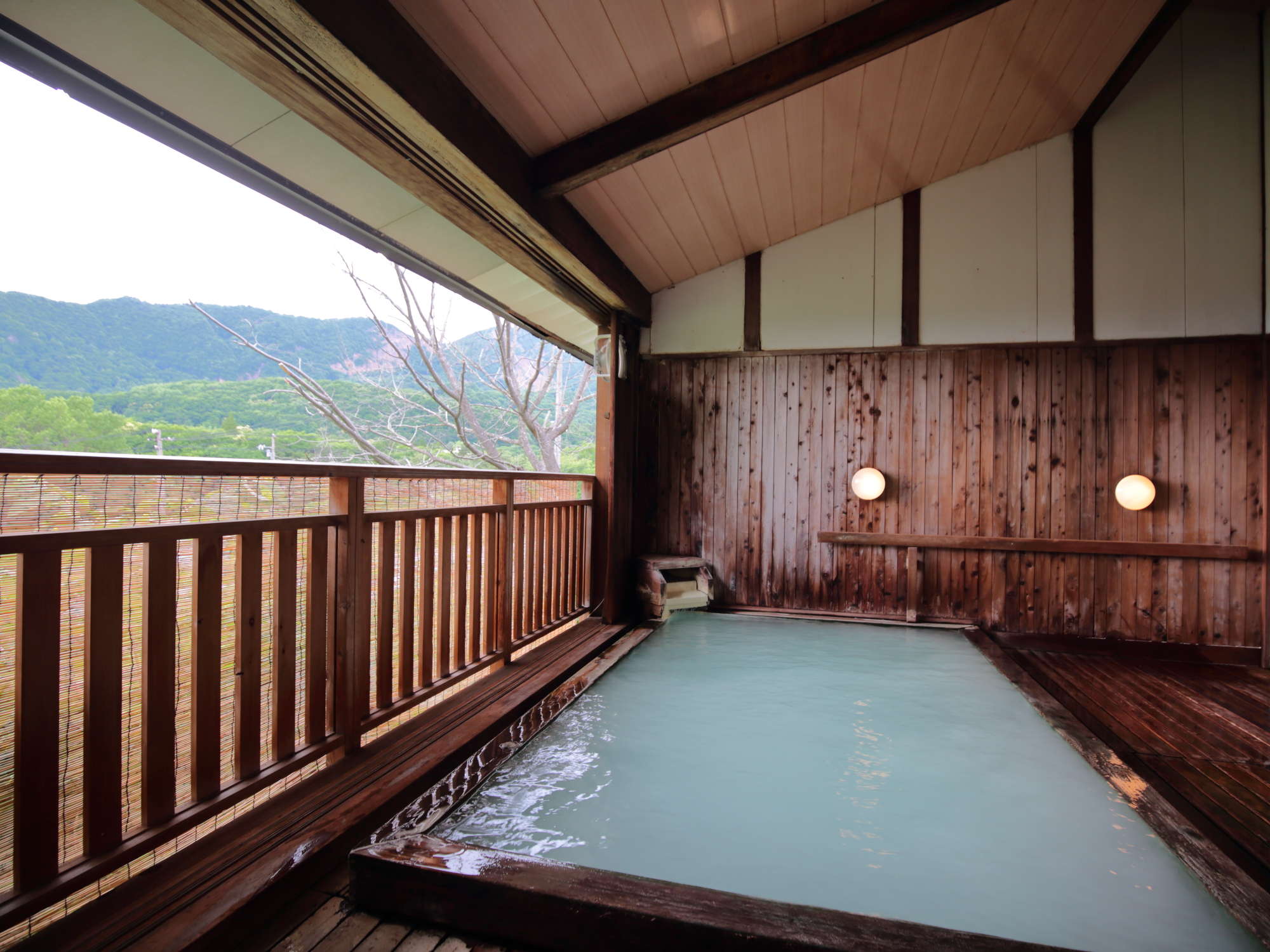 Open-air sulphur onsen bath with milky water and a wooden roof overlooking the Zao mountains at Hotel Matsukaneya Annex