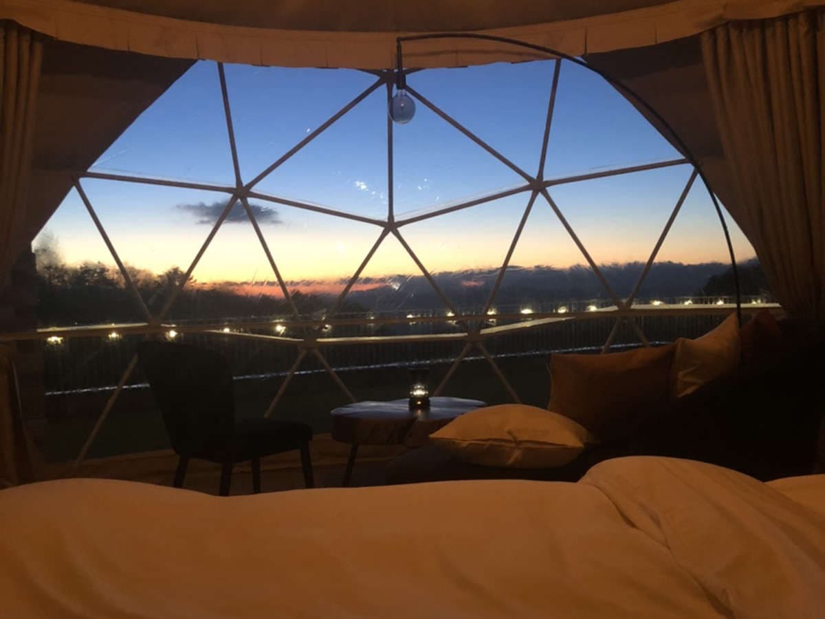 Interior of a glamping geodesic dome with a bed and lantern facing a sunset mountain view at Zao Onsen