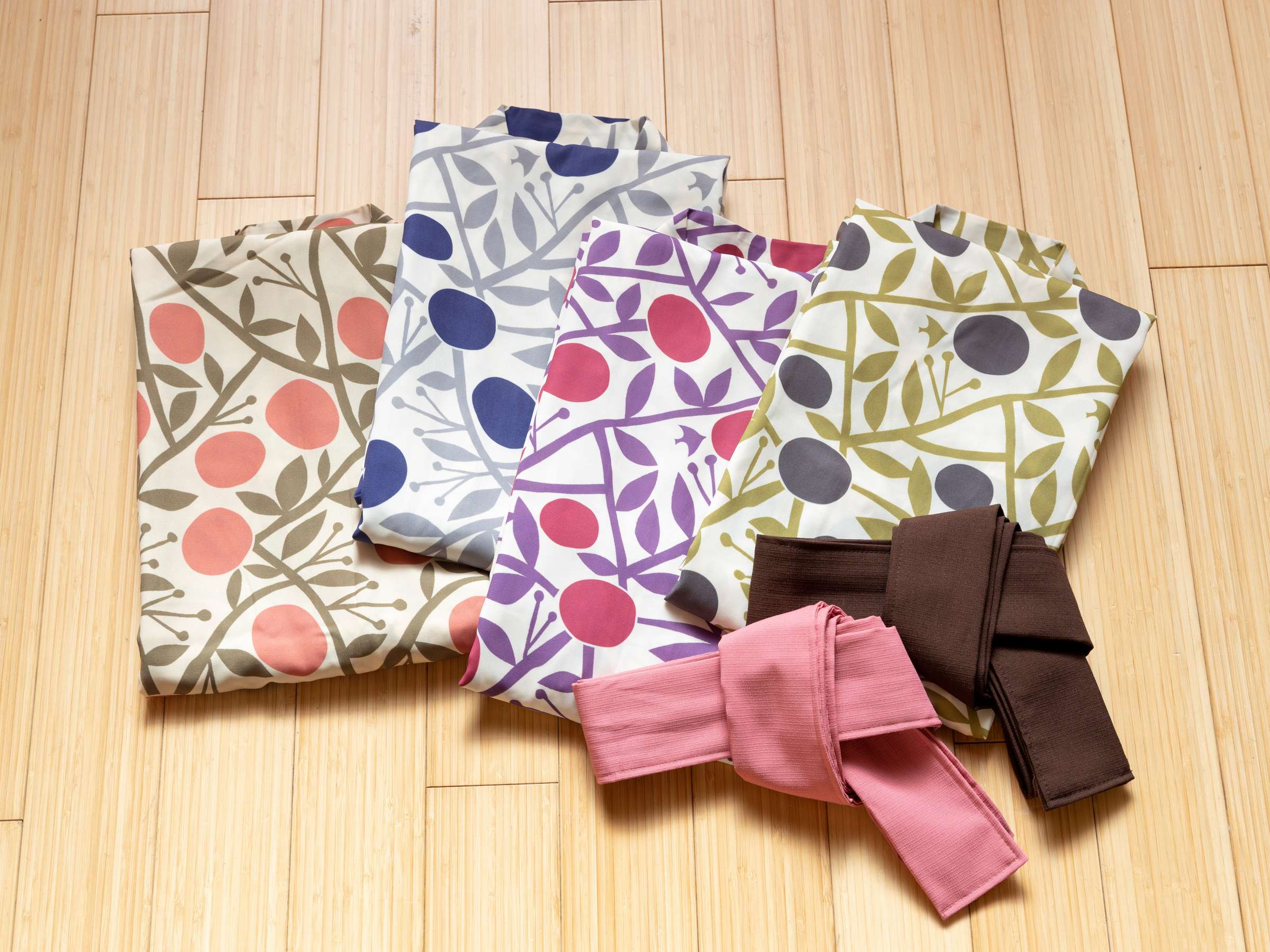 Set of patterned yukata robes with colorful obi belts laid out on a wooden floor