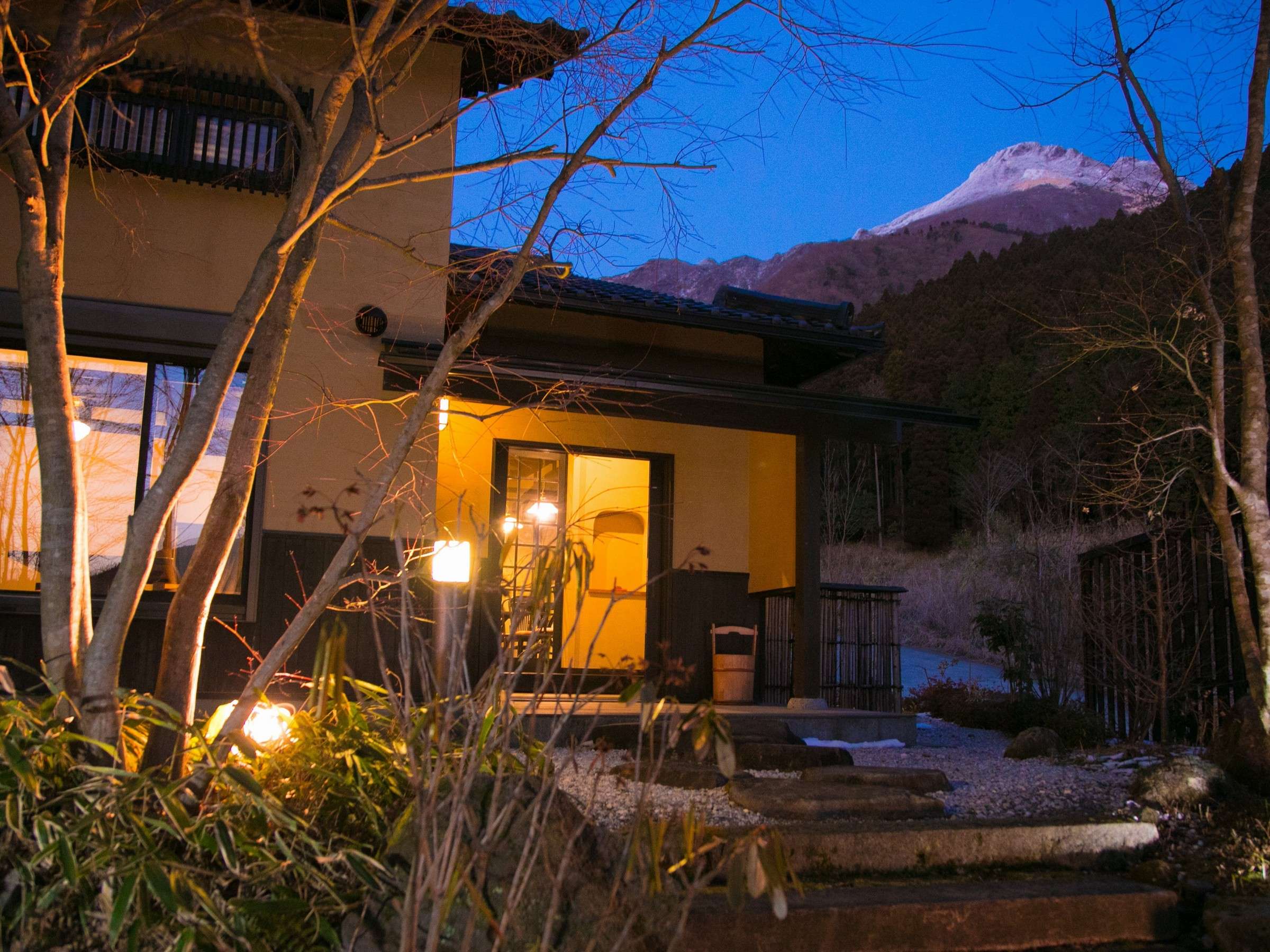 Yufuin Yufusaryo lit guest villa at dusk with the snow-capped peak of Mt Yufu rising behind in Yufuin Onsen
