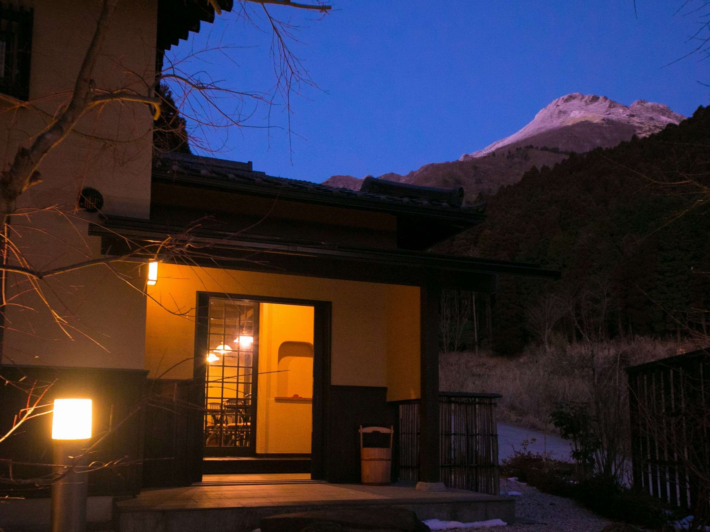 Exterior of a Yufuin Yufusaryo guest building glowing at night beneath the mountains of Yufuin