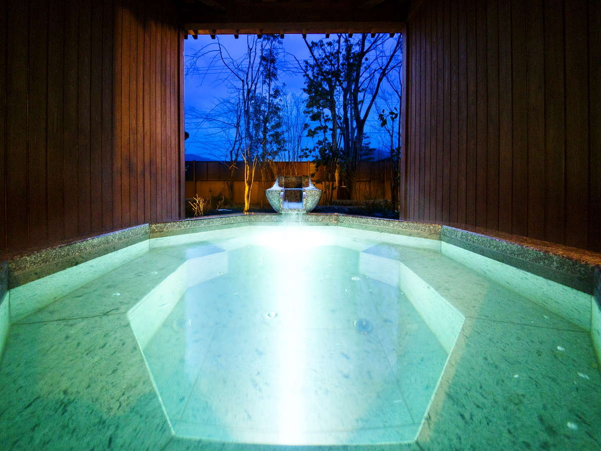 Private open-air stone bath glowing at dusk with a garden view at Kanazawa Yuwaku Onsen Hyakurakuso