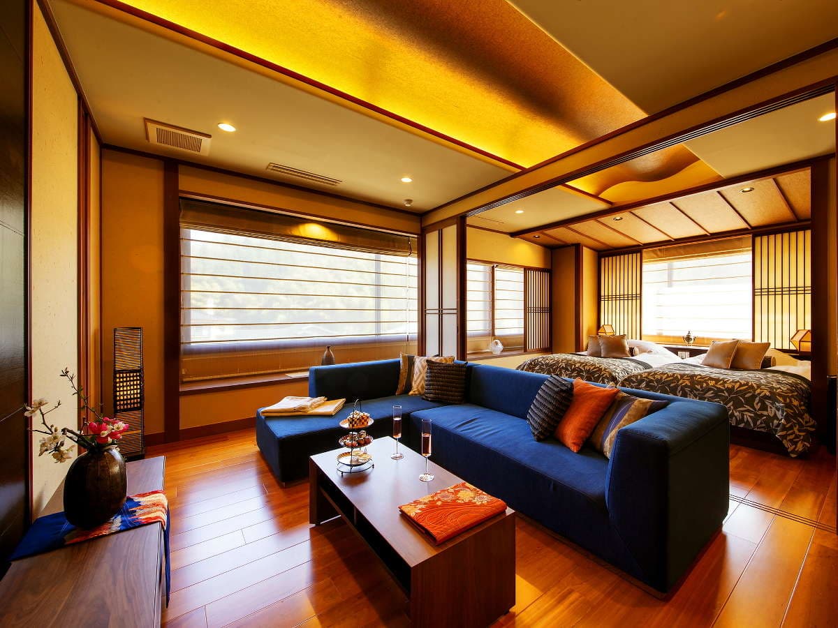 Spacious premium guest room with twin beds, blue sofa and mountain-view windows at Hyakurakuso, Yuwaku Onsen