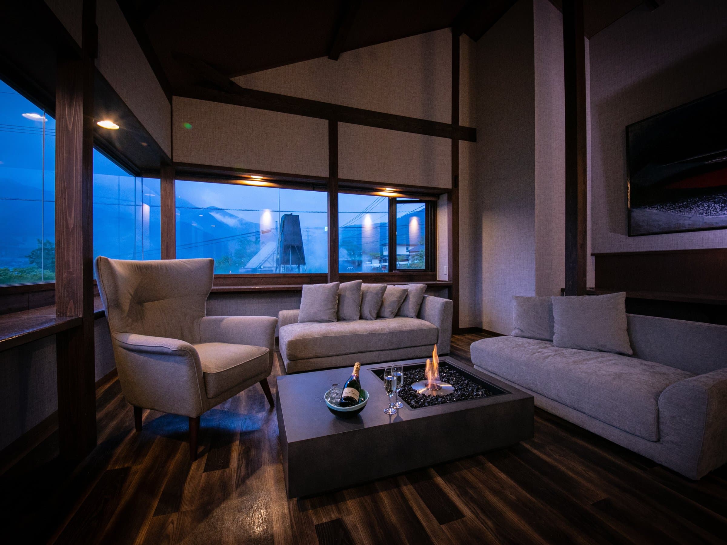 Spacious sitting room with sofas, a fireplace table and evening mountain view at Yufuin Kazenomori