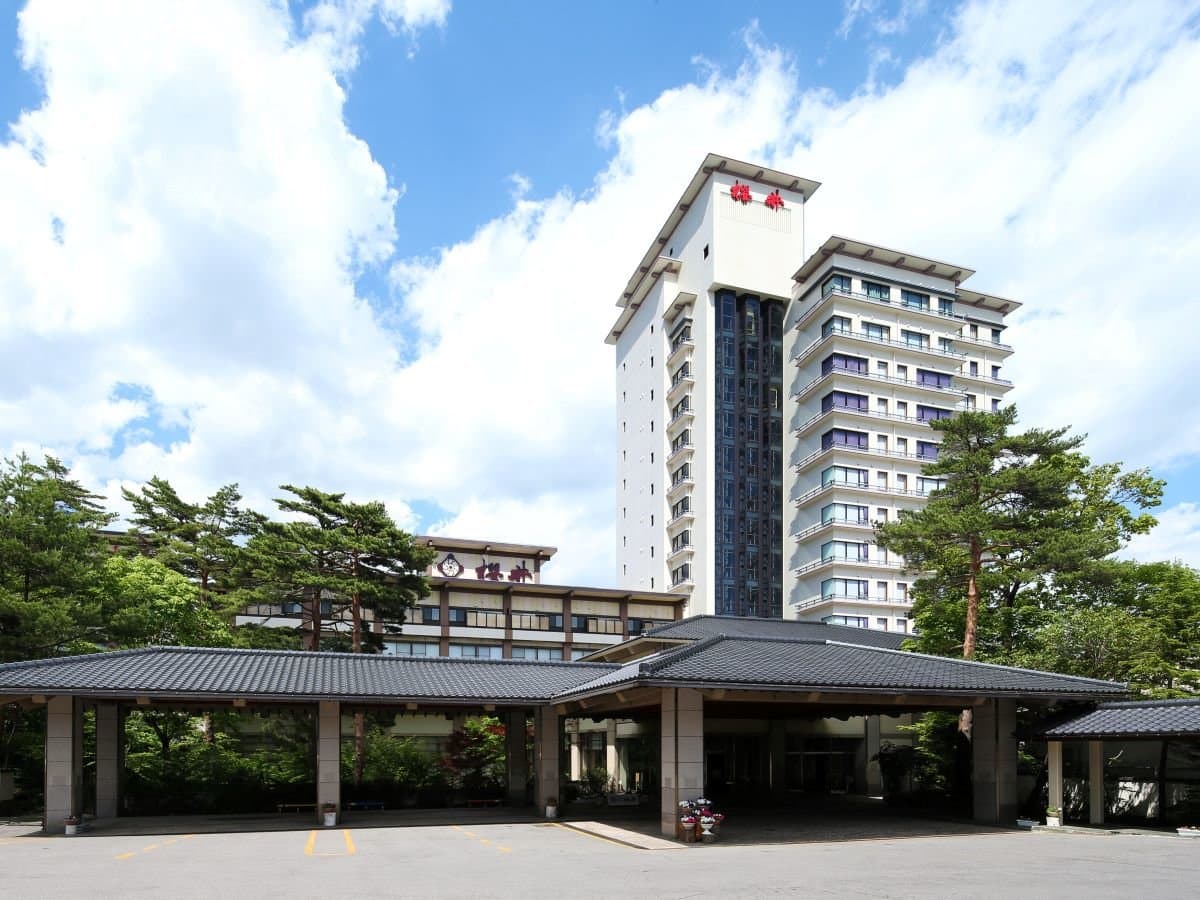 Hotel Sakurai main building exterior with the high-rise tower and tile-roofed entrance porch under a blue sky in Kusatsu Onsen