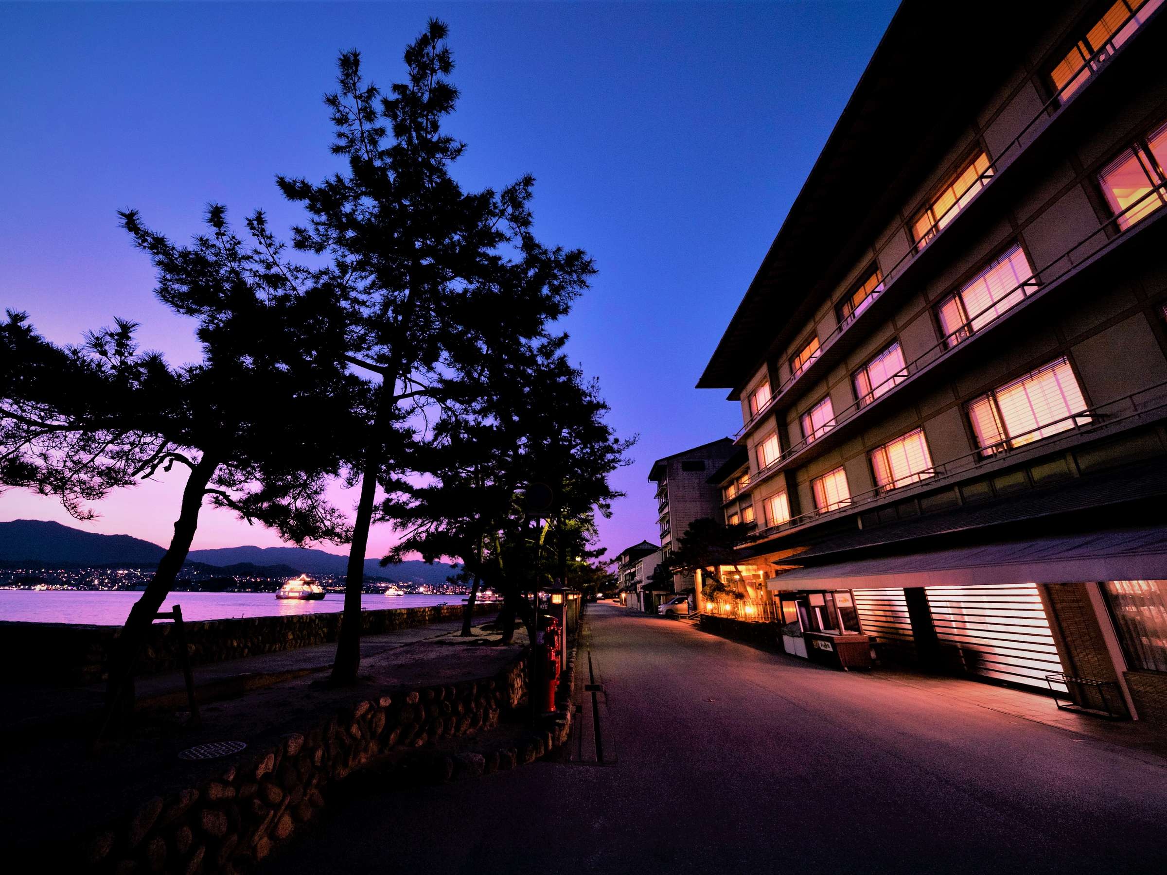 Hotel Miyarikyu seaside exterior at dusk with lit rooms and pine trees overlooking the Seto Inland Sea on Miyajima island