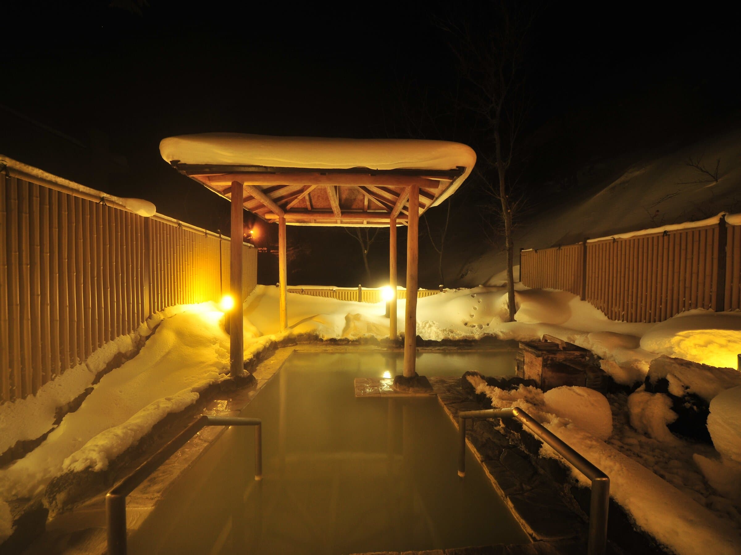 Snow-covered outdoor rotenburo lit by lanterns at night in winter at Yumoto Itaya, Okunikko Yumoto Onsen