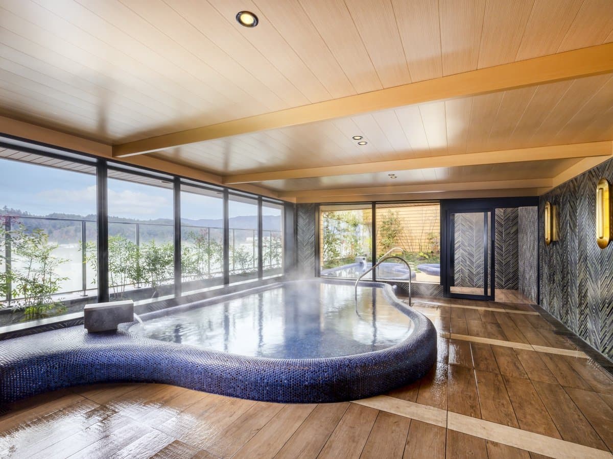 Indoor public onsen bath at Mercure Hida Takayama with deep blue mosaic tub, wood ceiling and large windows over the valley