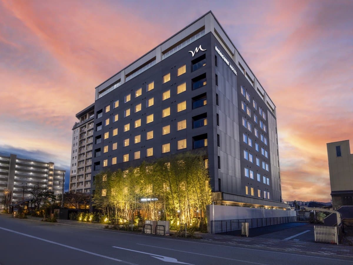Mercure Hida Takayama hotel exterior at dusk, dark facade glowing against a pink sunset sky with illuminated bamboo garden