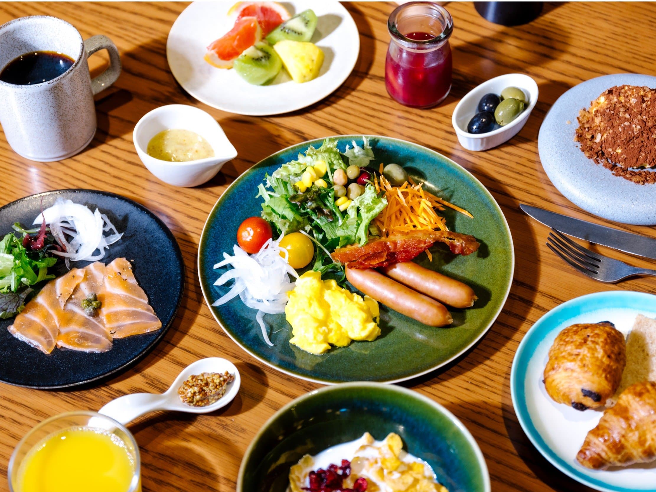 Breakfast spread with fresh salad, salmon, sausages, pastries, fruit and coffee on a wooden table