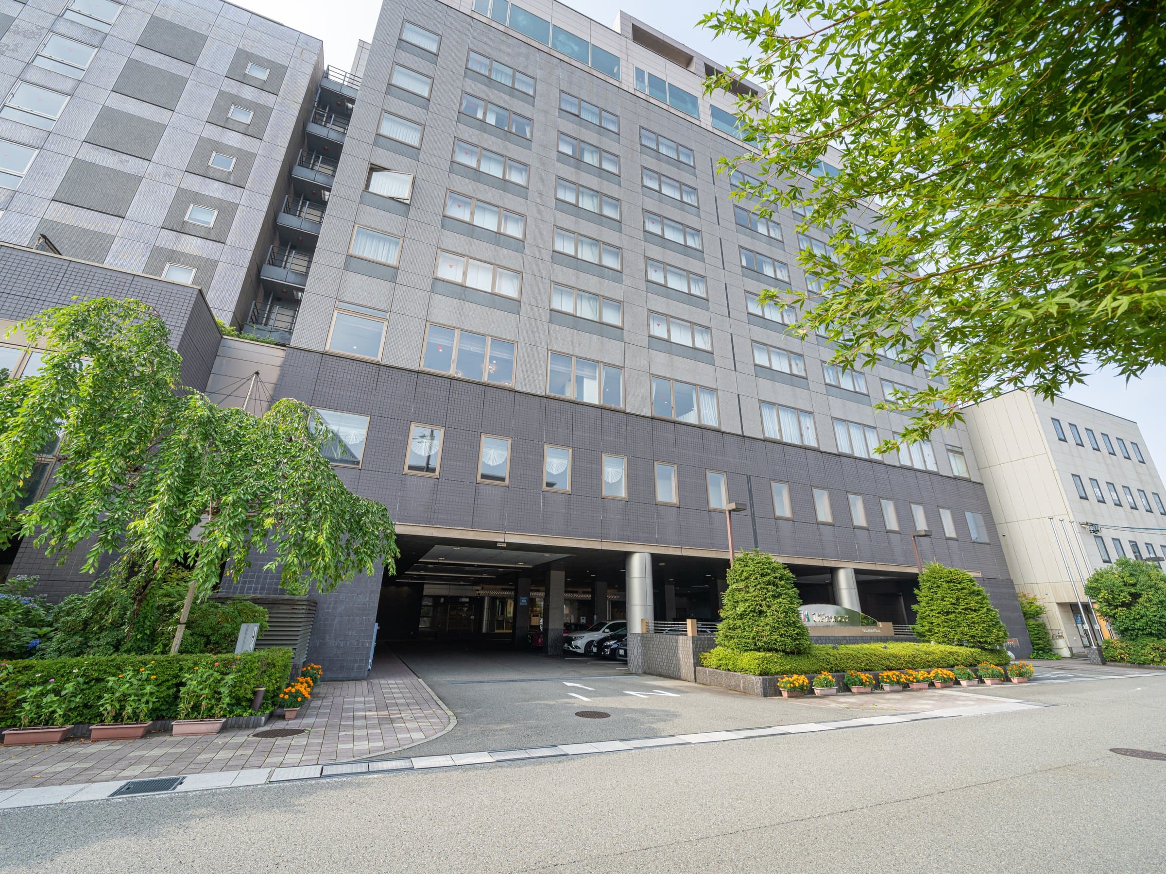 Exterior of Hida Hotel Plaza, a multi-storey Takayama Onsen hotel framed by trees and a landscaped entrance