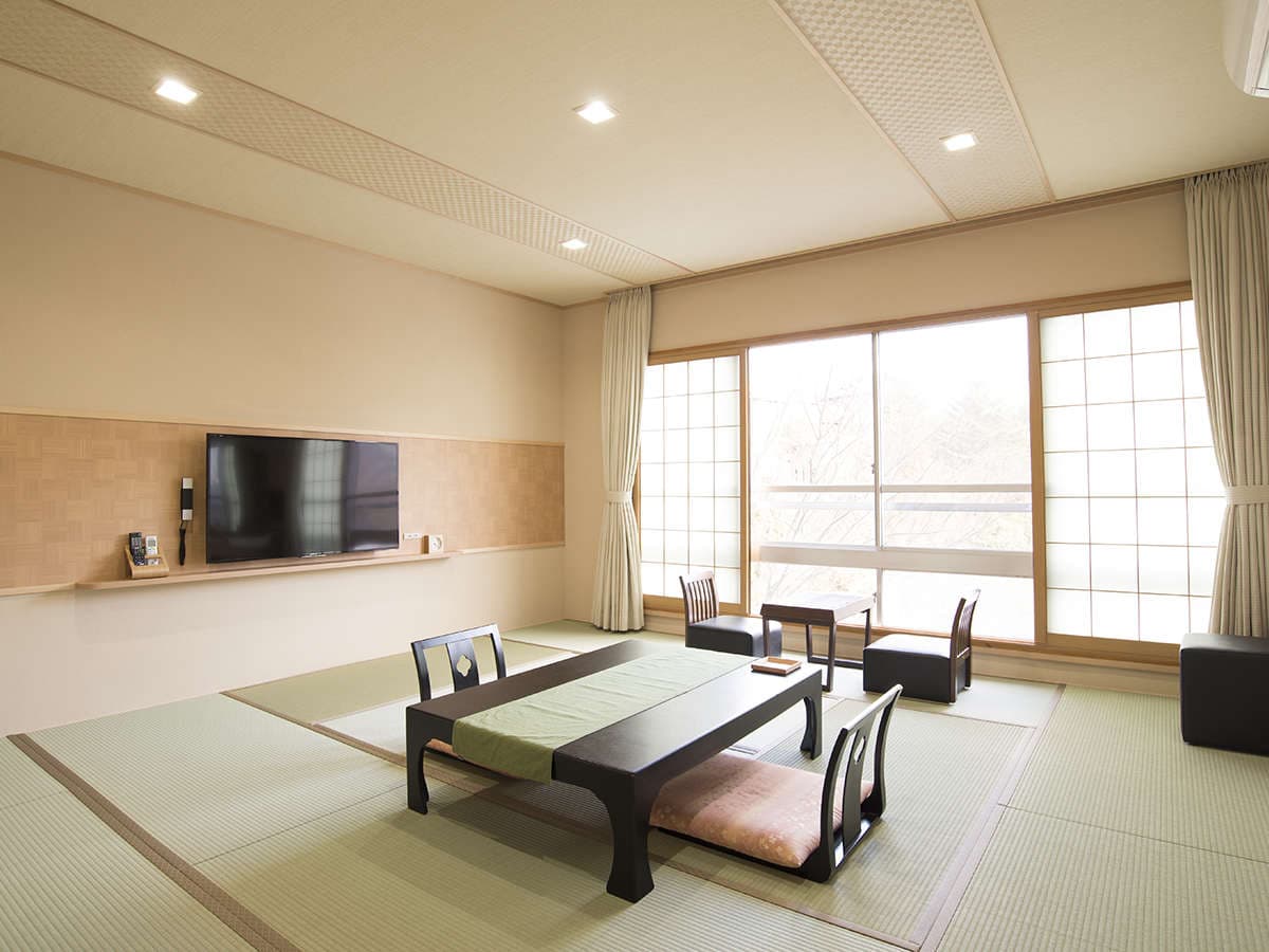 Spacious tatami guest room with a low dining table, floor chairs and shoji-screened windows framing the wooded mountainside at Motoyu Ryusenkaku, Arima Onsen