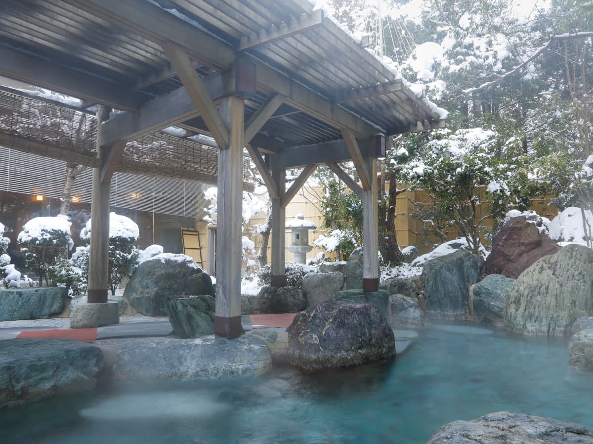 Snow-covered open-air rotenburo with steaming water and a timber pavilion at Takayama Green Hotel in winter