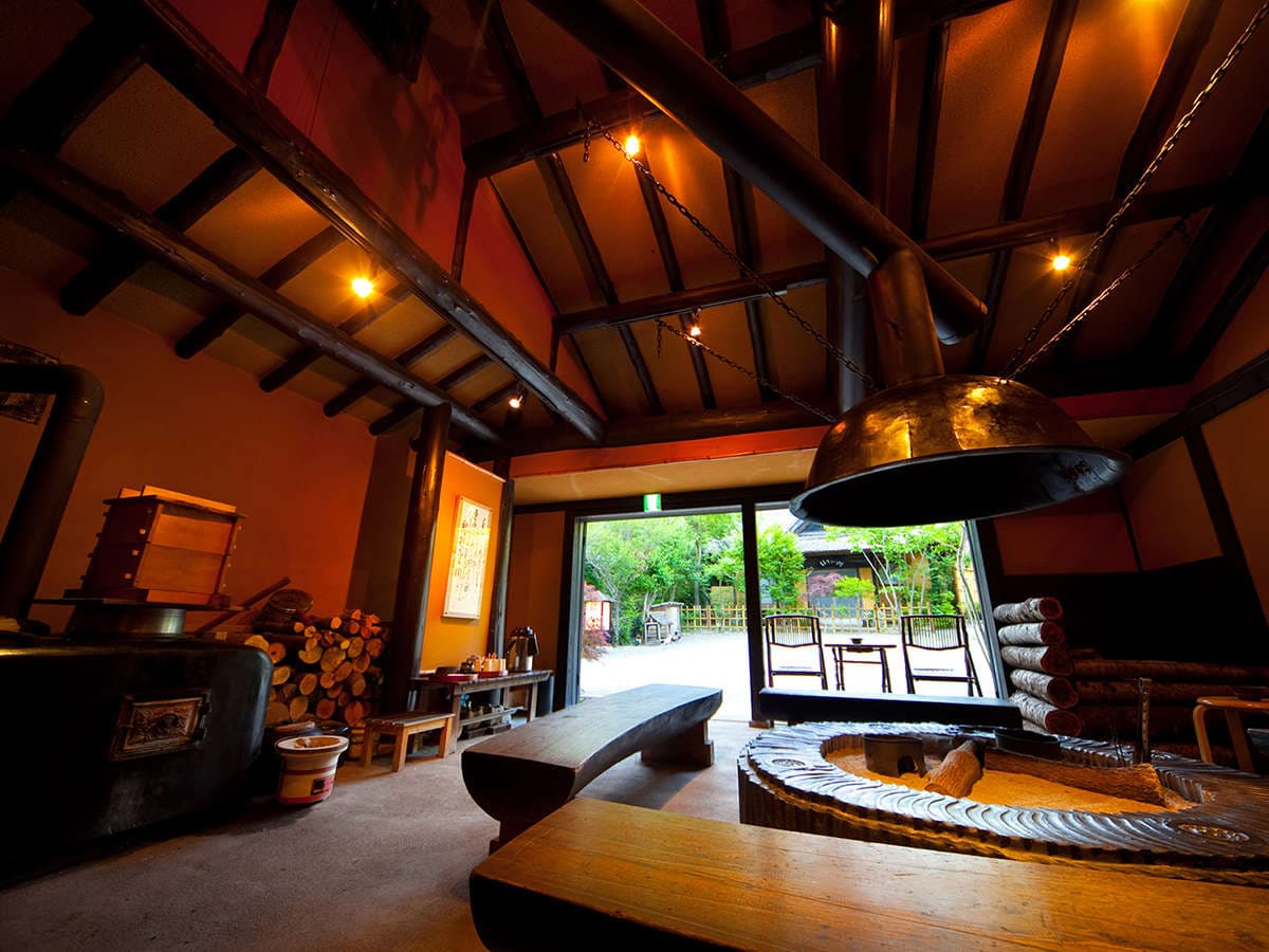 Rustic irori hearth lounge at Yufuin Hoteiya with exposed beams, a wood stove and garden view