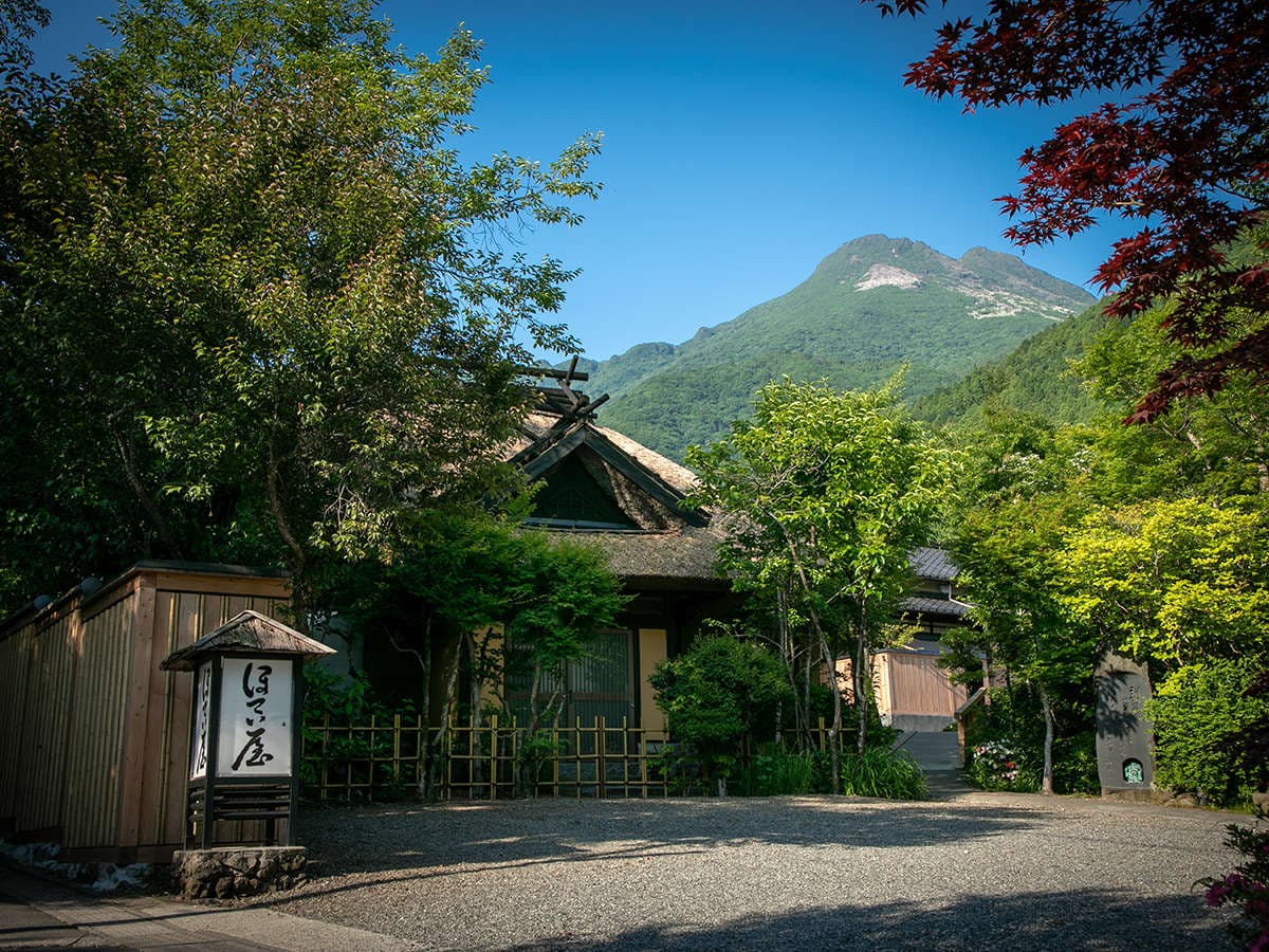 Yufuin Hoteiya thatched-roof ryokan buildings framed by maples with Mount Yufu rising behind in Yufuin Onsen