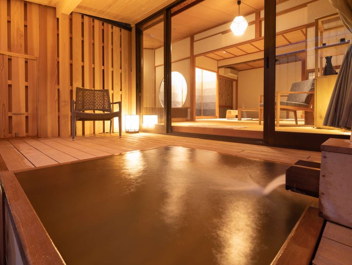 Private open-air cypress bath glowing at dusk beside a tatami room at Yunode Ryokan, Yuwaku Onsen near Kanazawa