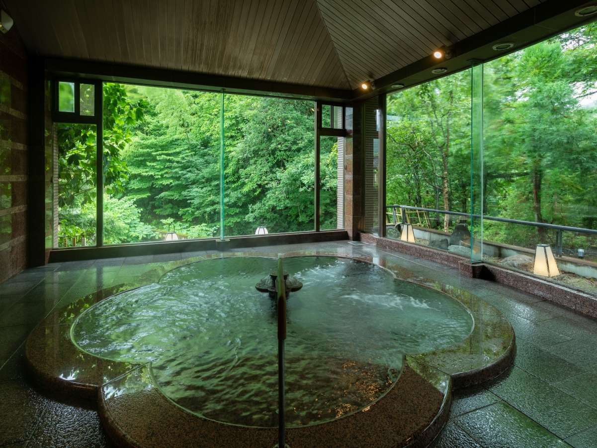 Indoor hot-spring bath with a plum-shaped red granite tub and forest views through glass walls at Yunode Ryokan