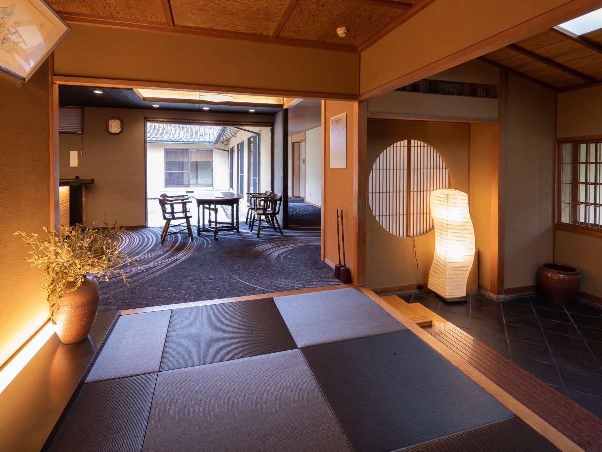 Warm lobby lounge with a paper andon lamp, round shoji window and chabudai tables by an inner courtyard at Yunode Ryokan