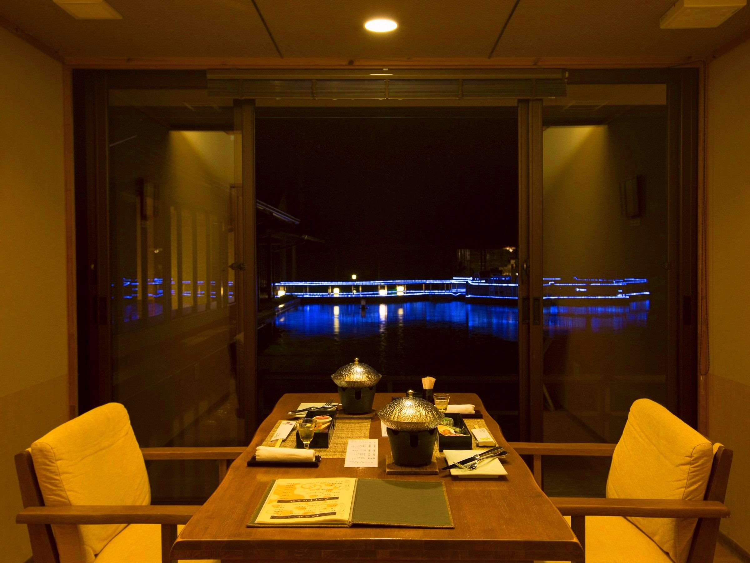 Private in-room dining table set with covered hotpots facing the illuminated night pool at Yurian, Ibusuki Onsen