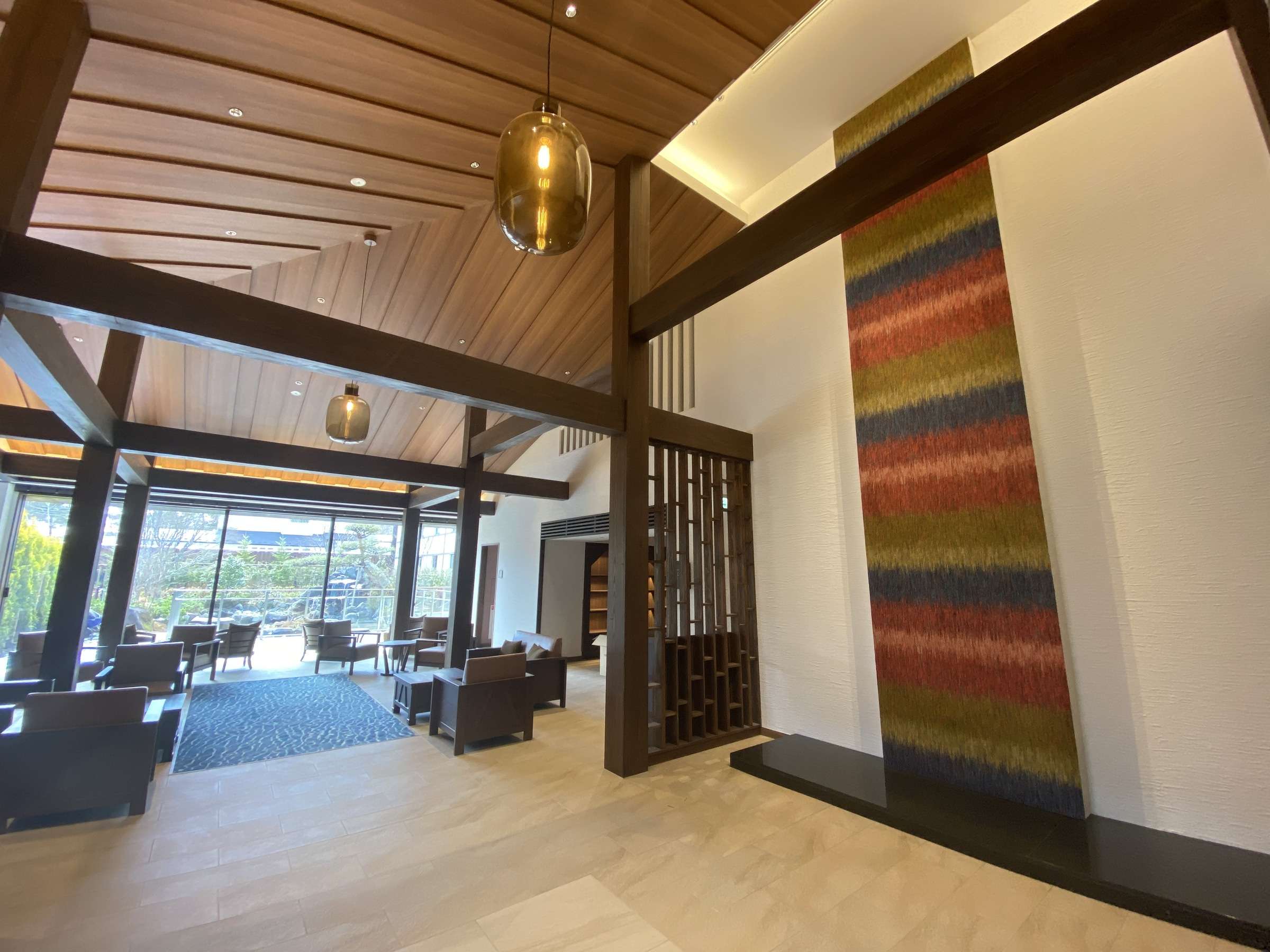 Entrance hall of La Vista Kusatsu Hills with exposed wooden beams, a glass pendant lamp and a striped textile wall hanging