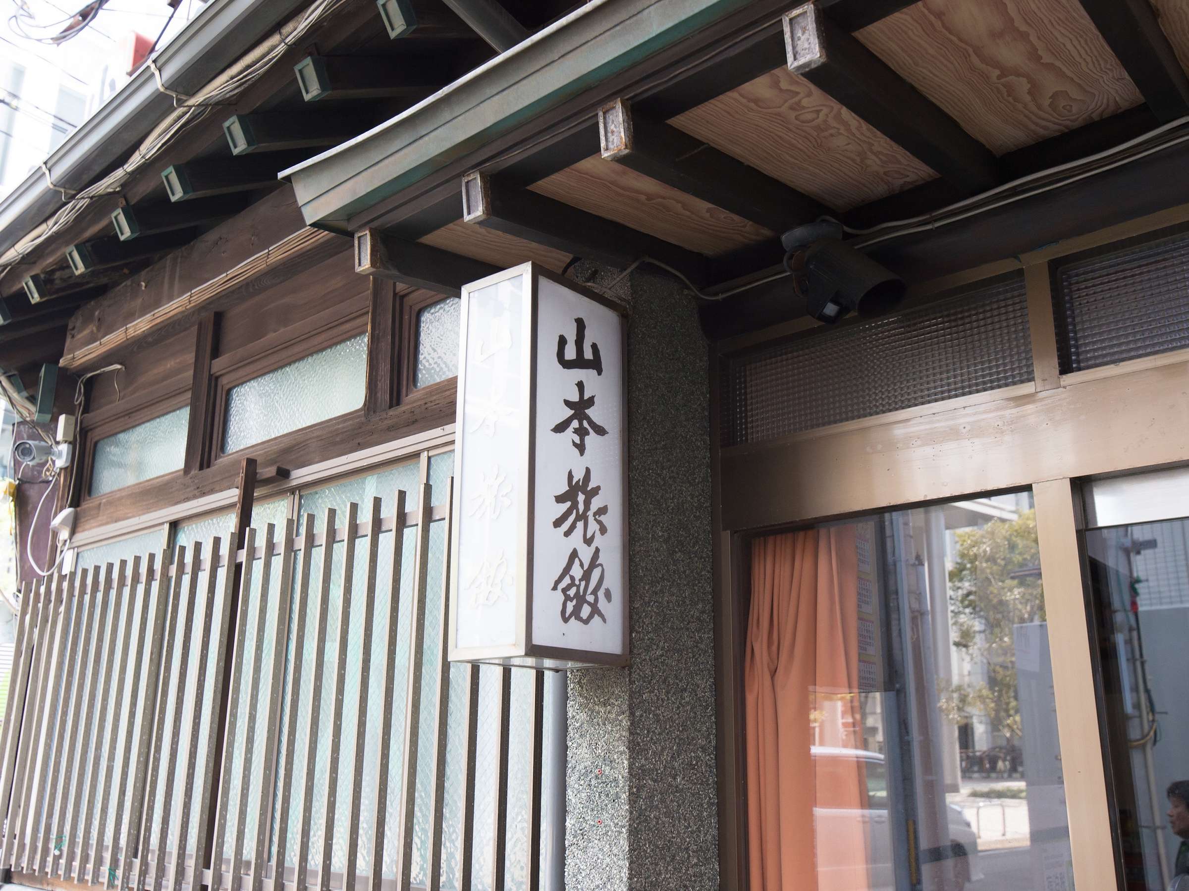 Close-up of the carved wooden eaves and illuminated vertical name sign reading Yamamoto Ryokan above the entrance