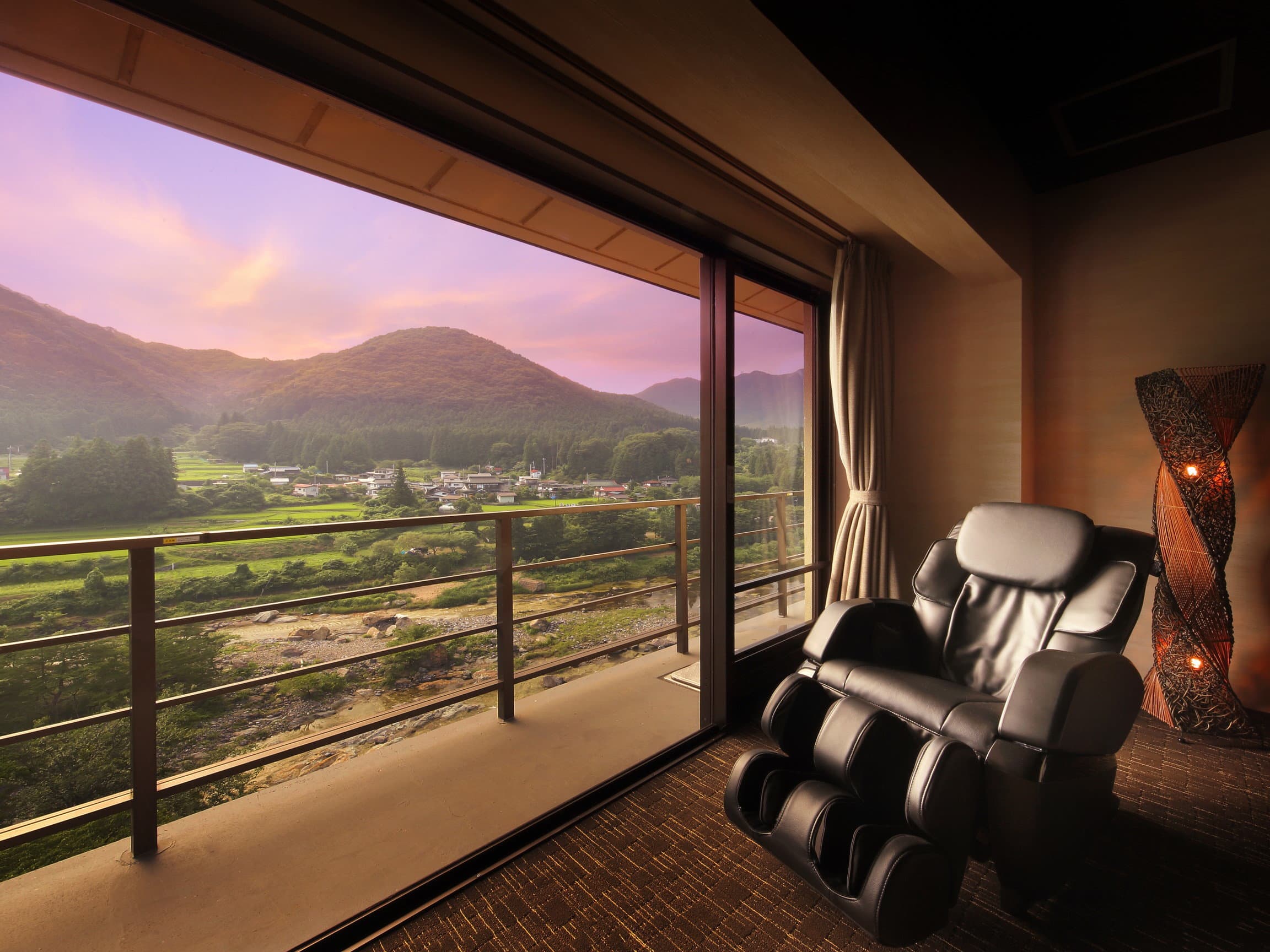 Guest room with massage chair and floor-to-ceiling window overlooking river valley and mountains at sunset, Wakatake no Sho Kinugawa