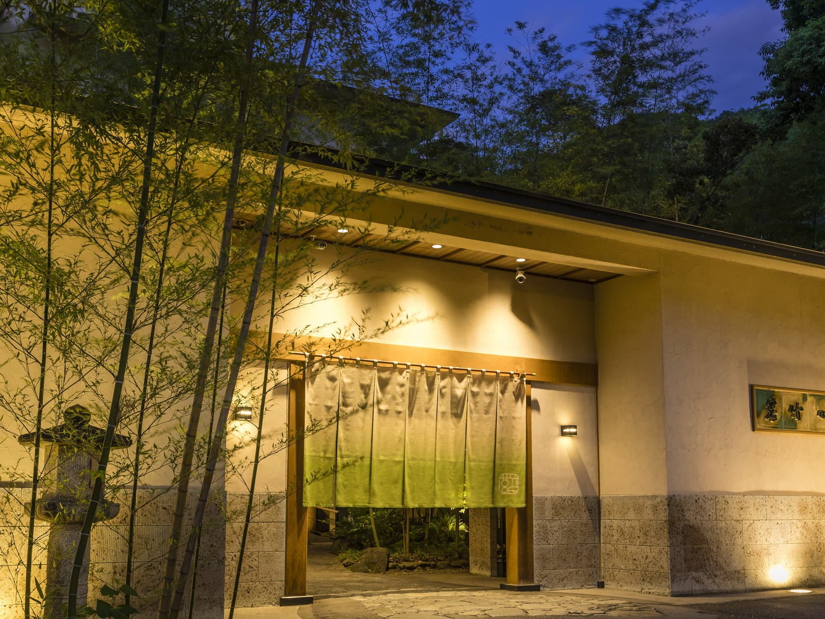 Wakatake no Sho ryokan illuminated entrance with green noren curtain framed by bamboo at dusk in Kinugawa Onsen, Nikko