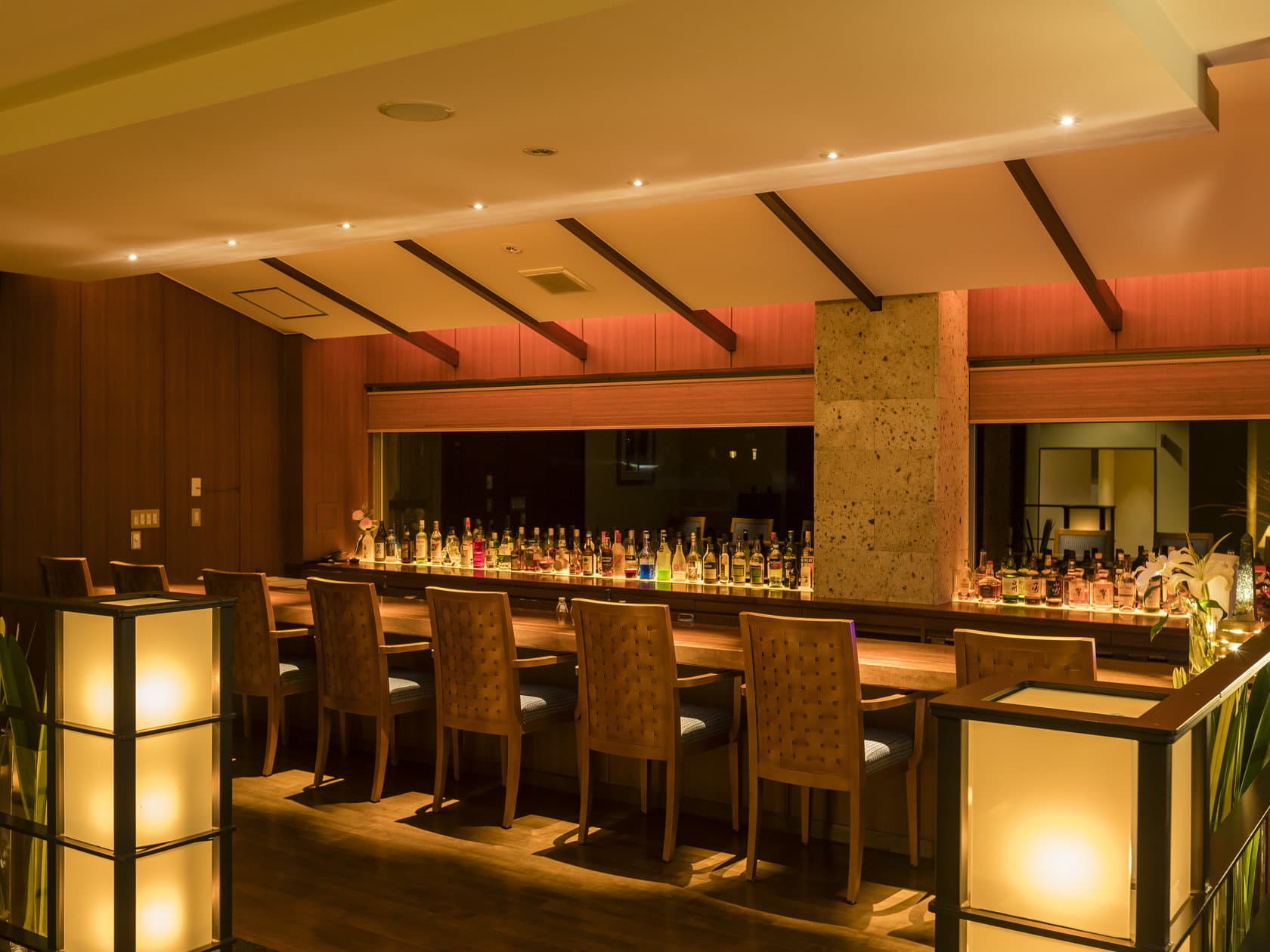 Warmly lit bar counter lined with bottles and lantern-style lamps in the evening at Wakatake no Sho ryokan, Nikko