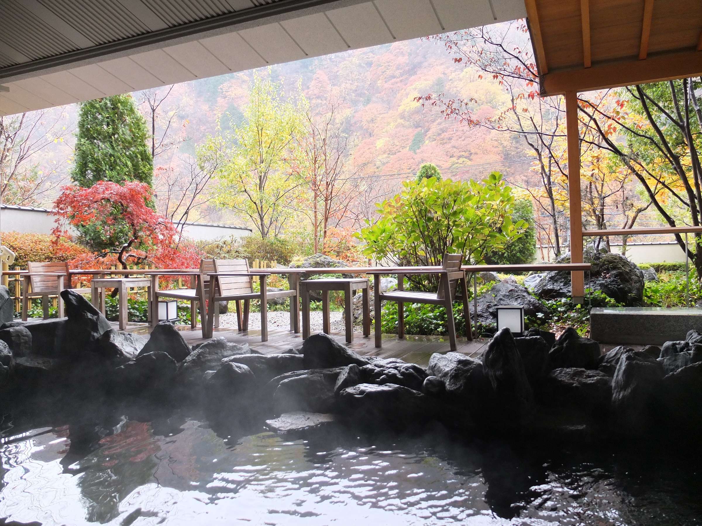 Open-air rotenburo bath set among black rocks with autumn foliage and lounge seating at Nikko Senhime Monogatari