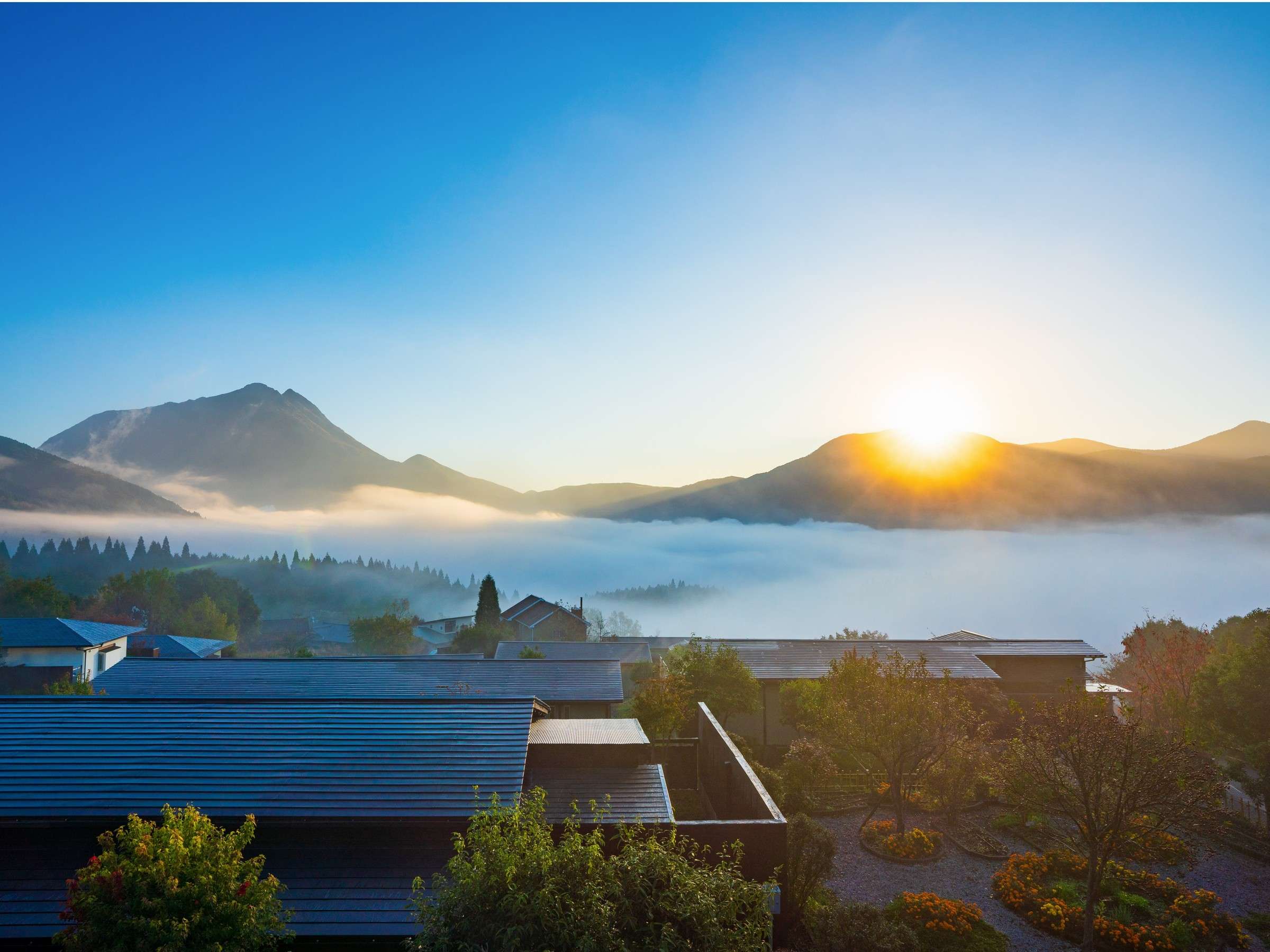 Yufuin Hanayoshi rooftops emerging from morning mist with Mount Yufu and the Yufuin basin behind