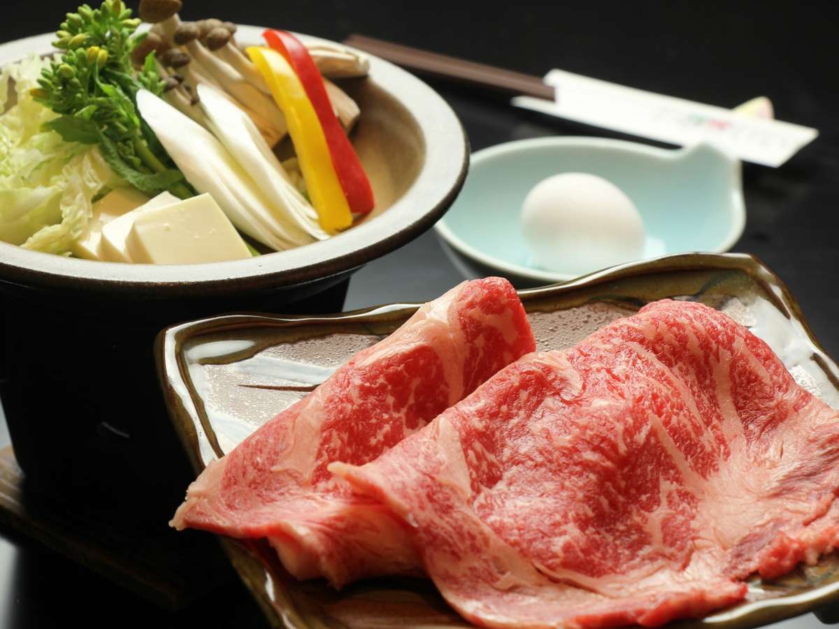 Sukiyaki-style set with sliced marbled beef, a hot pot of vegetables and tofu, and a raw dipping egg