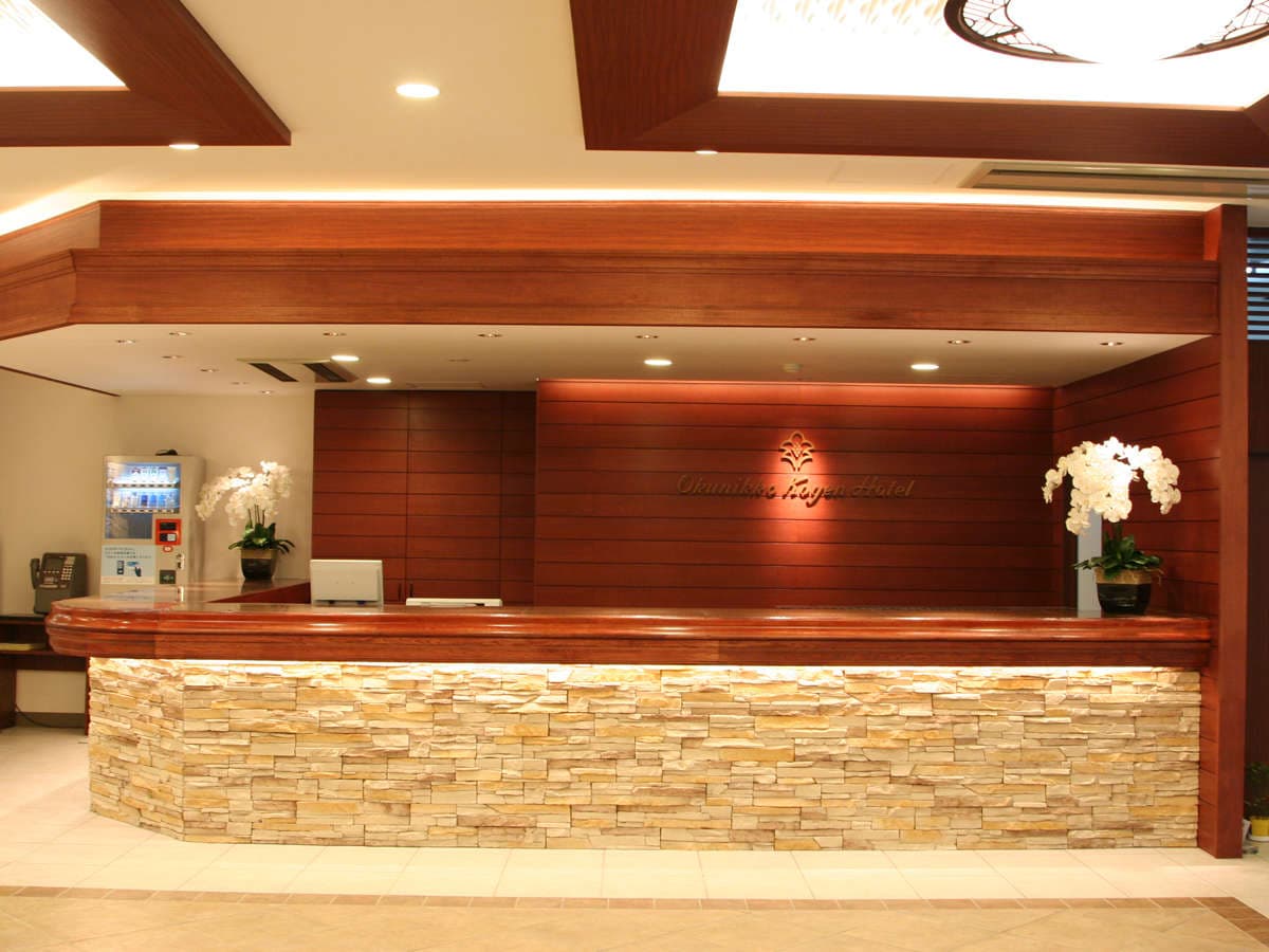 Front desk and lobby of Okunikko Kogen Hotel with warm wood paneling, stone-clad counter and orchid arrangements