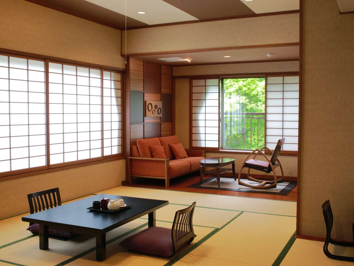 Traditional tatami guest room at Okunikko Kogen Hotel with shoji screens, low table and orange sofa overlooking forest greenery