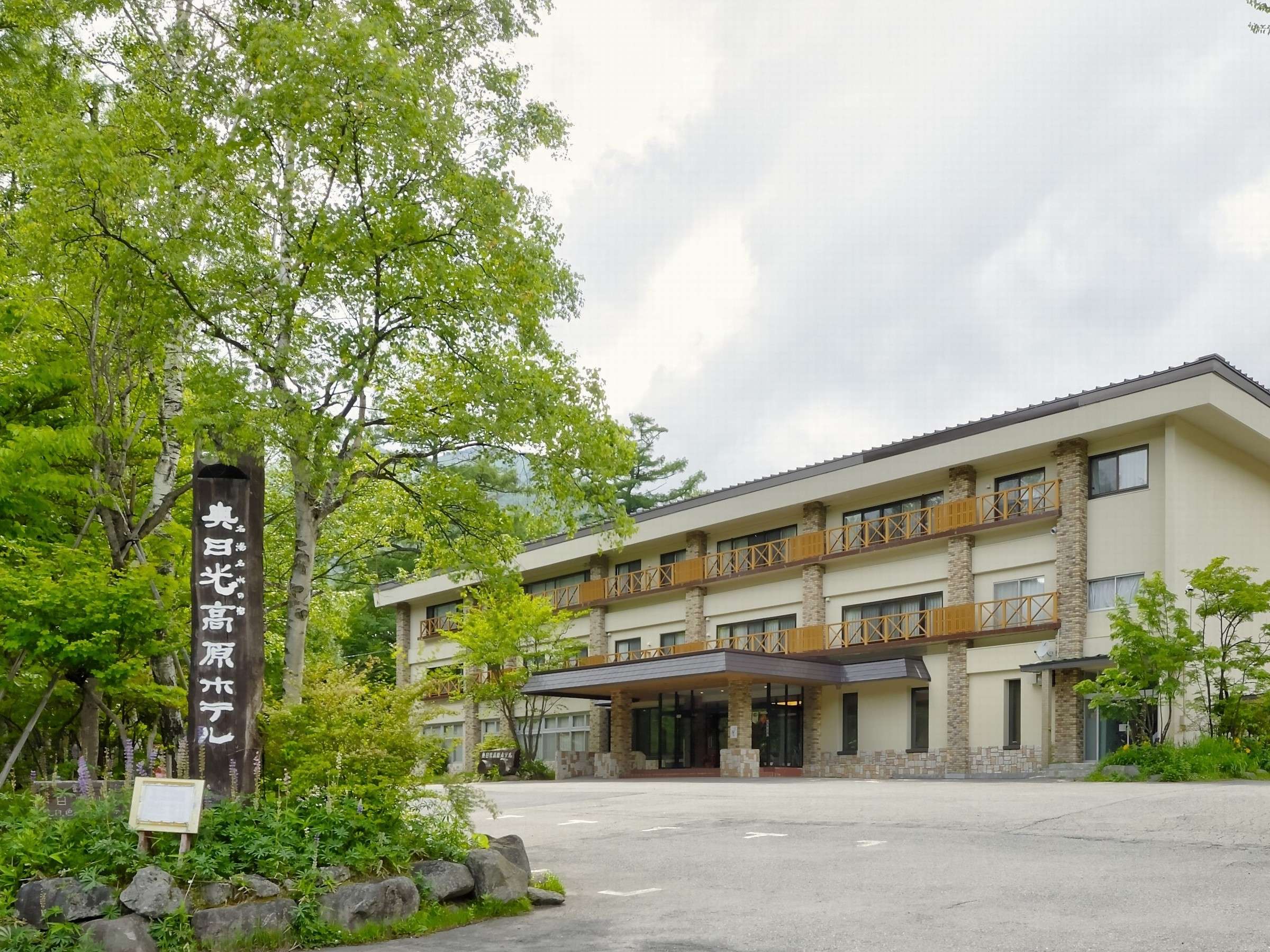 Okunikko Kogen Hotel exterior, a three-storey building with stone facade and wooden balconies framed by green trees in Okunikko, Nikko