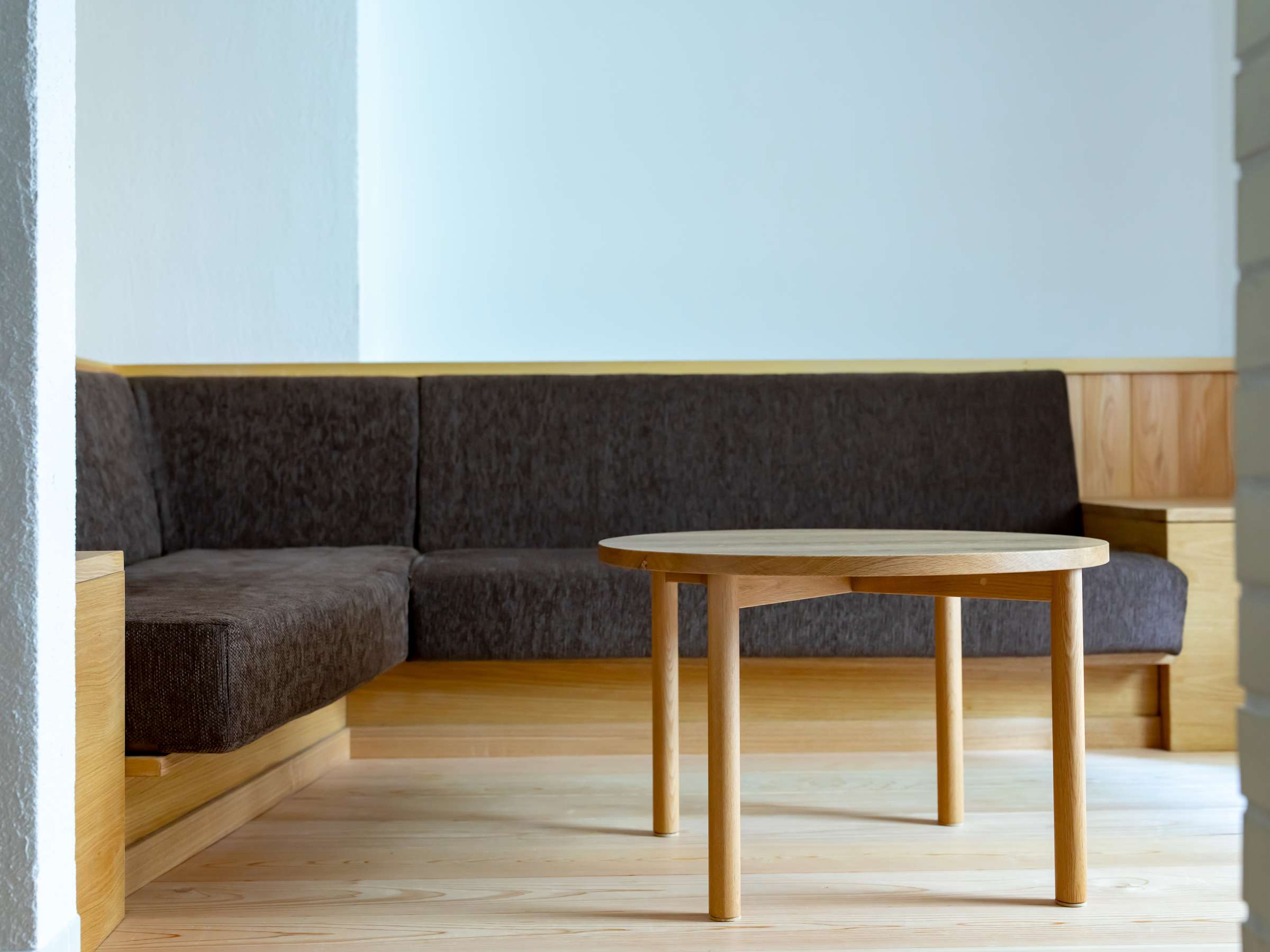Quiet lounge nook with a charcoal upholstered bench and round cedar table, Sensui, Kinosaki Onsen