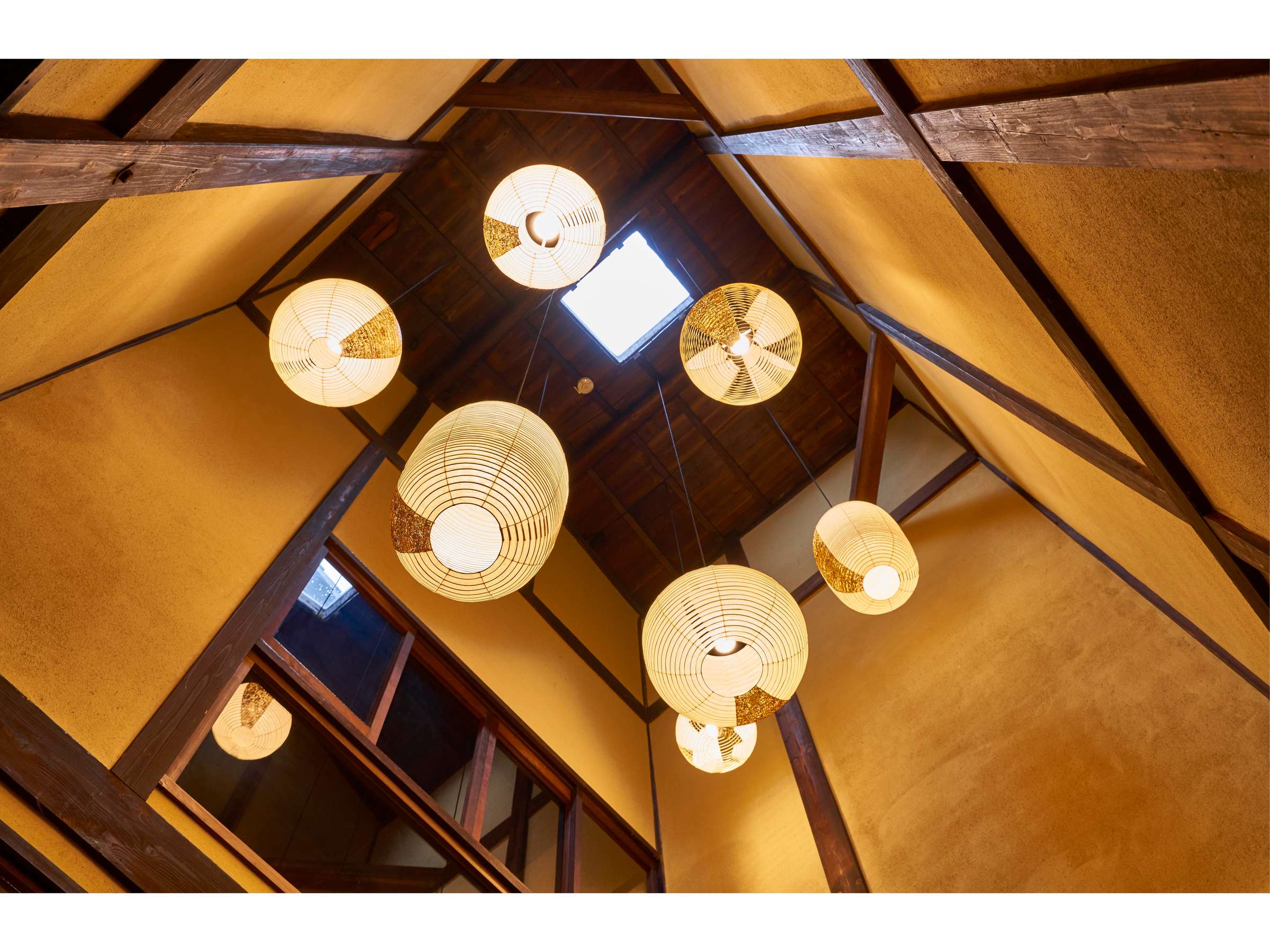 Interior architectural detail at Zen-Oyado Nishitei looking up at clustered washi paper lantern lights among exposed timber roof beams