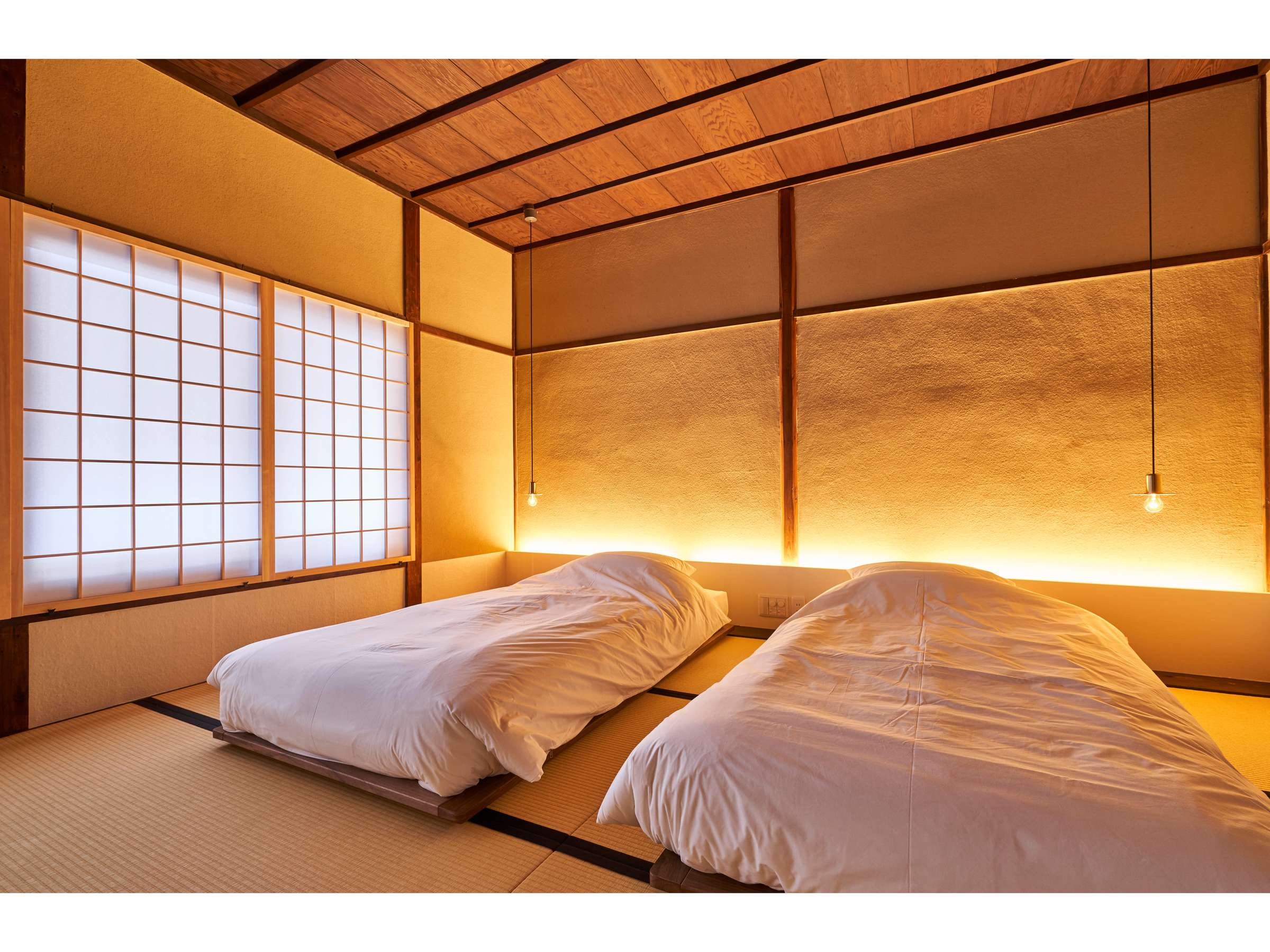 Tatami guest room at Zen-Oyado Nishitei with two futons made up, shoji paper screens and a softly backlit gold-leaf wall